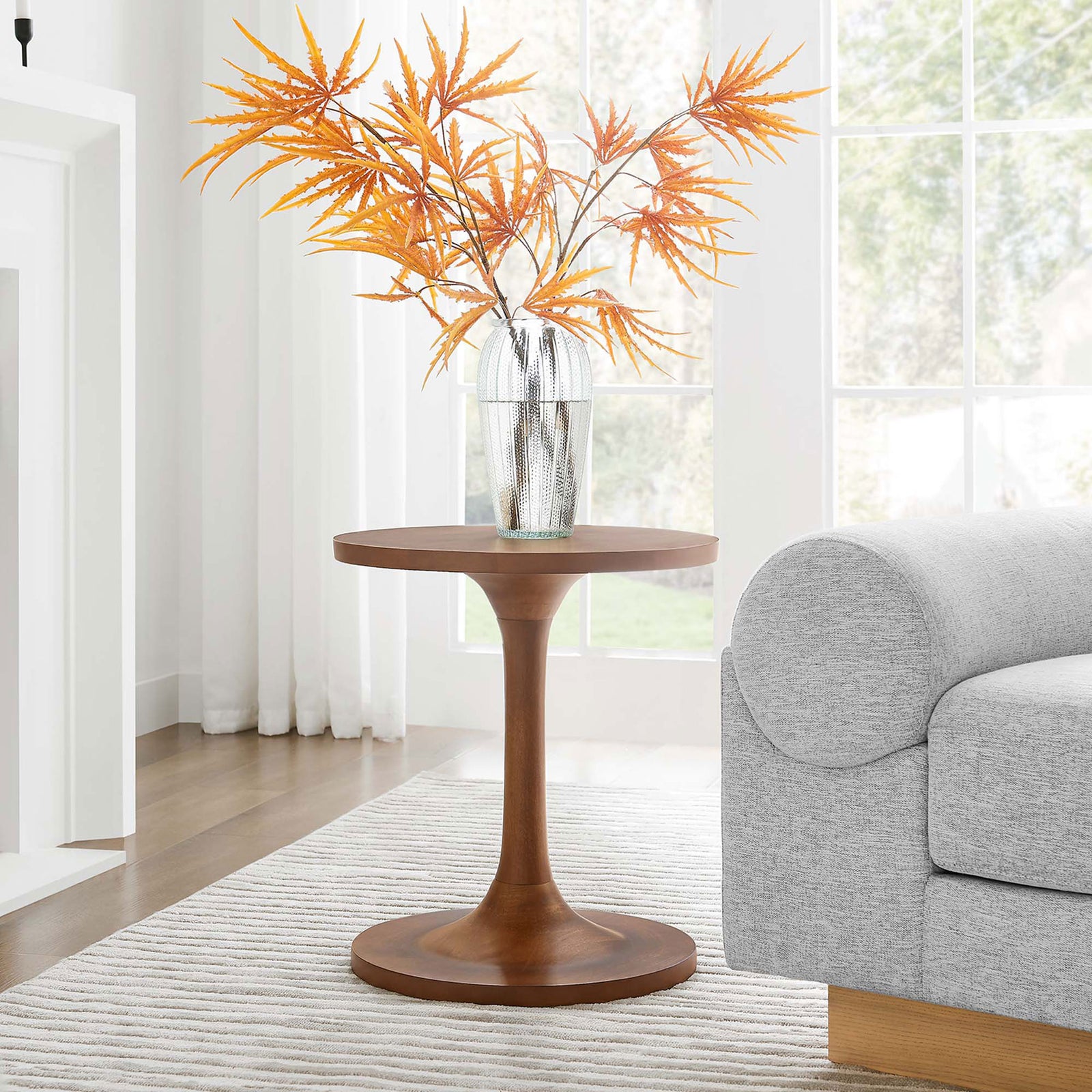 Lina round walnut side table beside a modern sofa, styled with a glass vase and autumn foliage || EEI-6573-WAL || front_angle_room