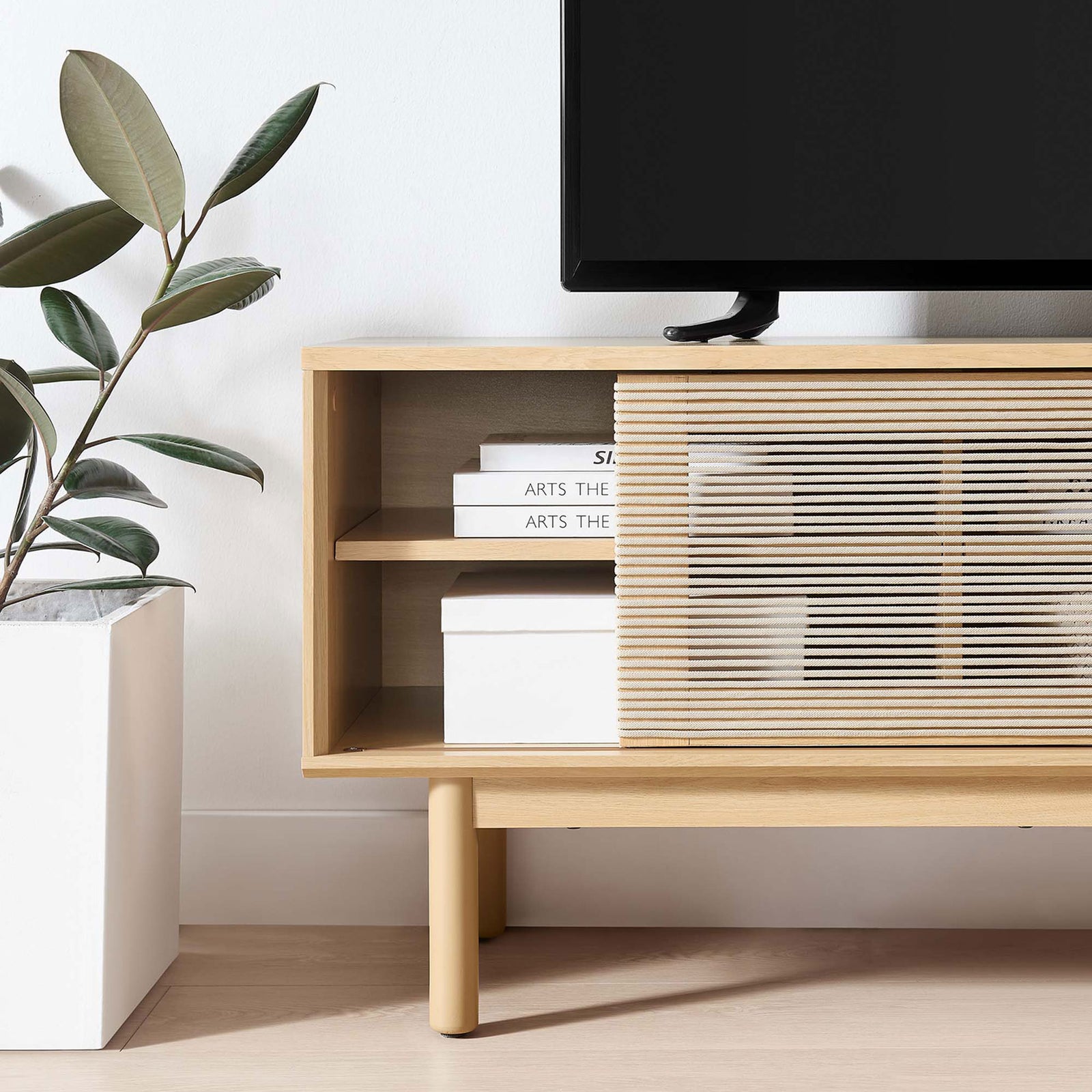 Milo TV stand styled in a bright living room with open shelves holding books and boxes beside woven rope door || EEI-6584-OAK-TAN || storage_open_room