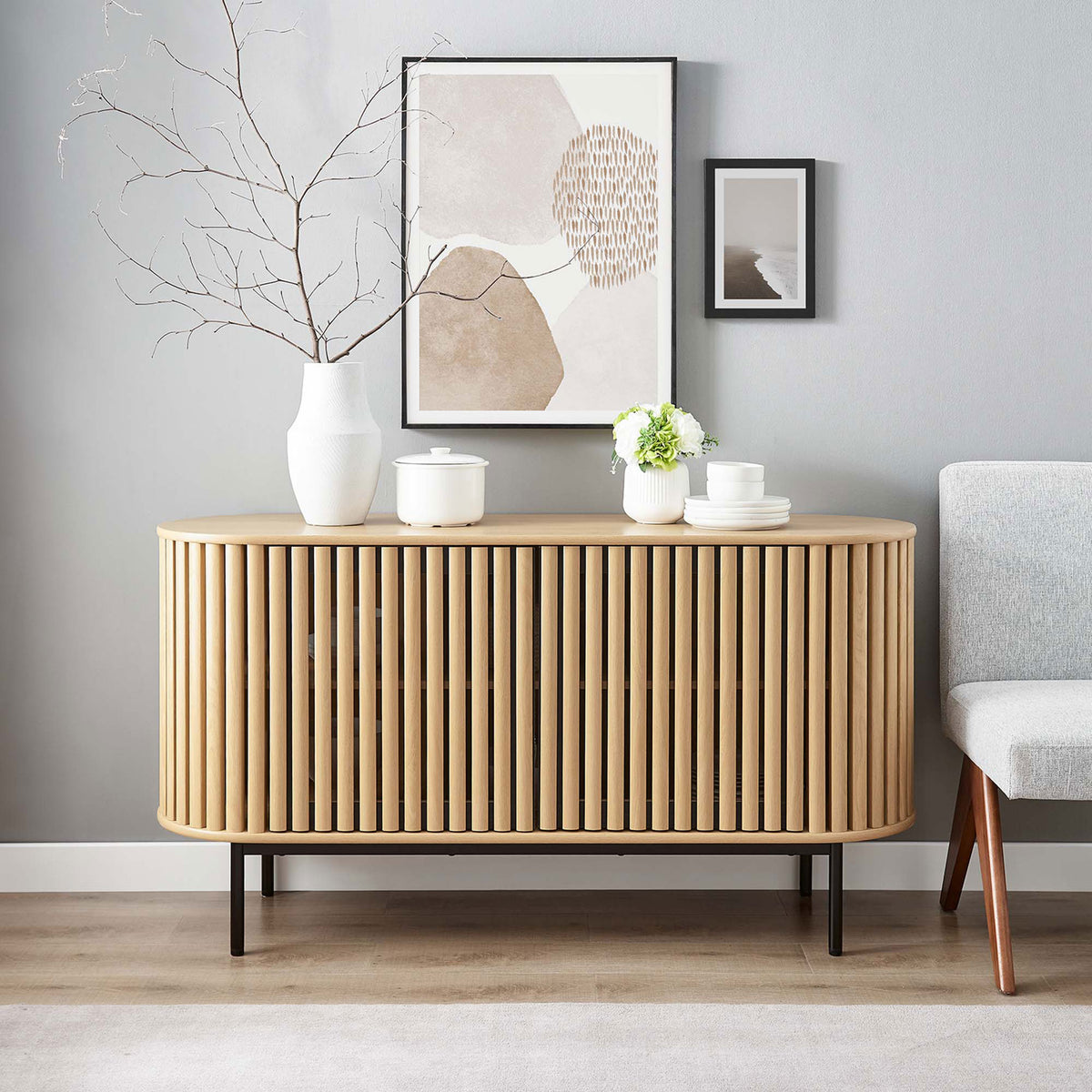 Fortitude oval sideboard in a modern living room styled with minimalist art and ceramic decor on top. || EEI-6590-OAK || front_room