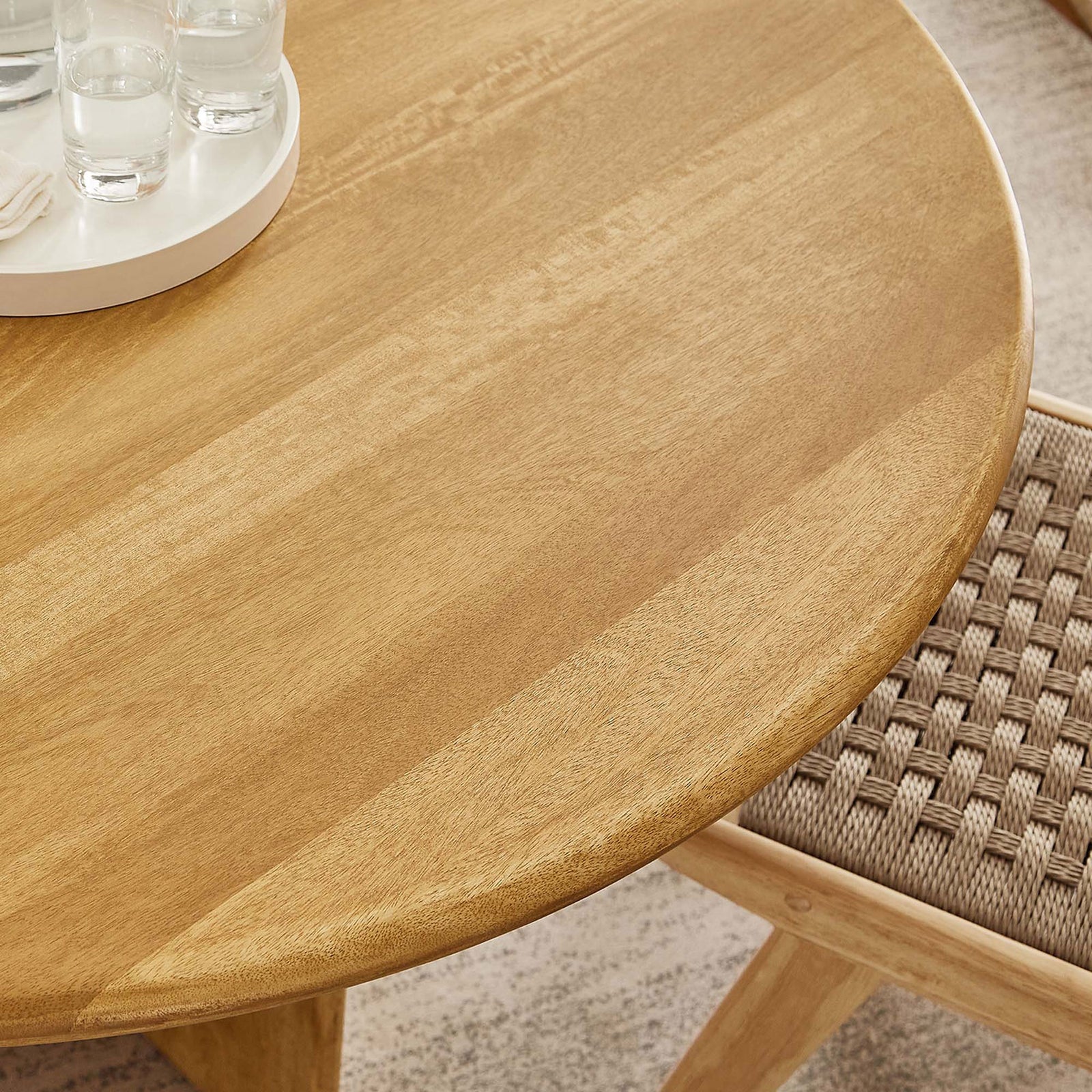 Round oak tabletop styled with glassware and a woven chair, showing the table in a warm modern dining space || EEI-6592-OAK || detail_room