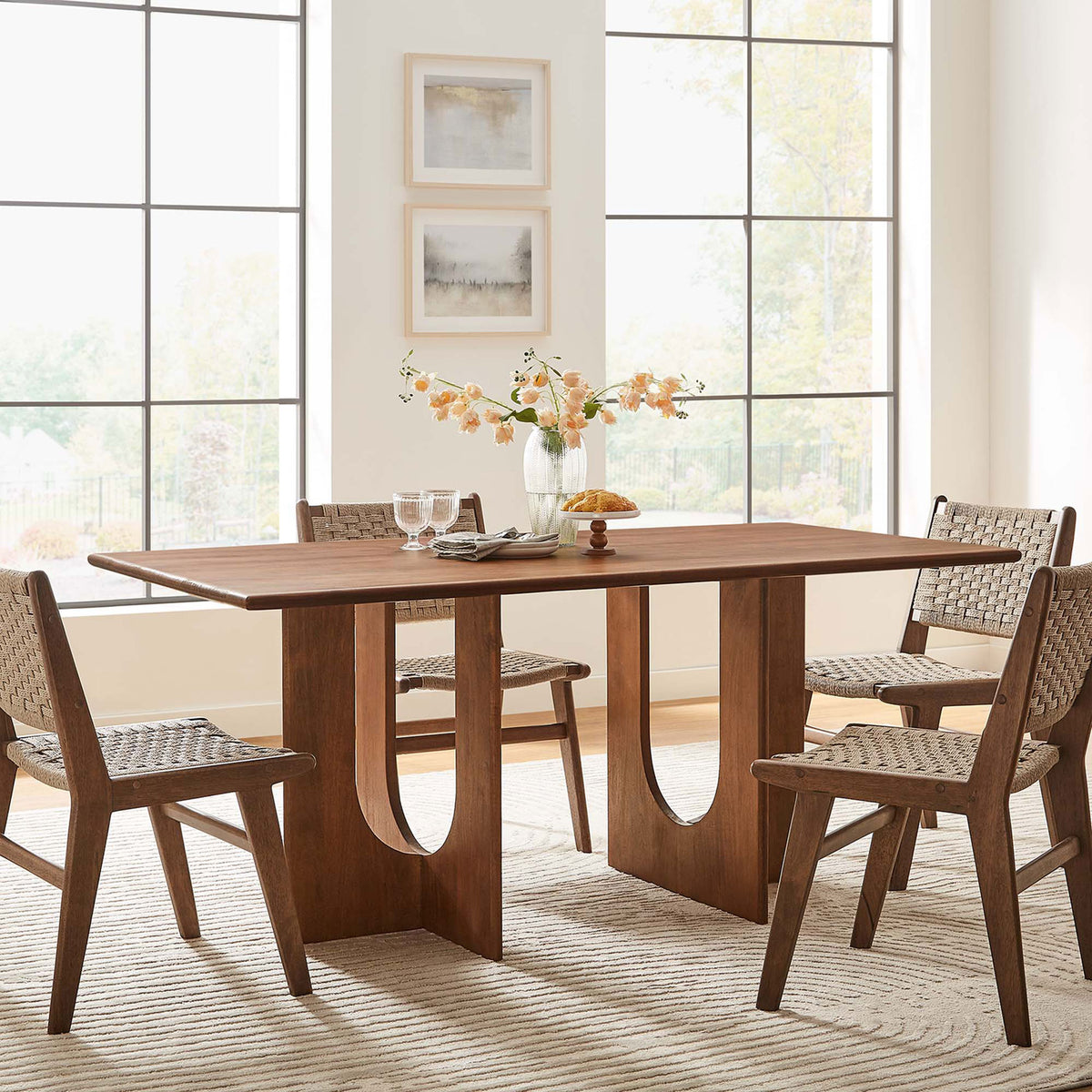 Rivian dining table anchoring a modern space, pairing its sculptural walnut base with coordinating woven chairs || EEI-6593-WAL || front_angle_room