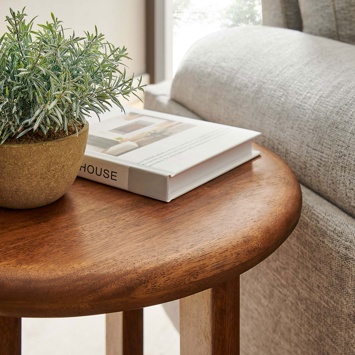 Round walnut tabletop styled beside a sofa with book and planter to show warm finish in use || EEI-6595-WAL || detail_room