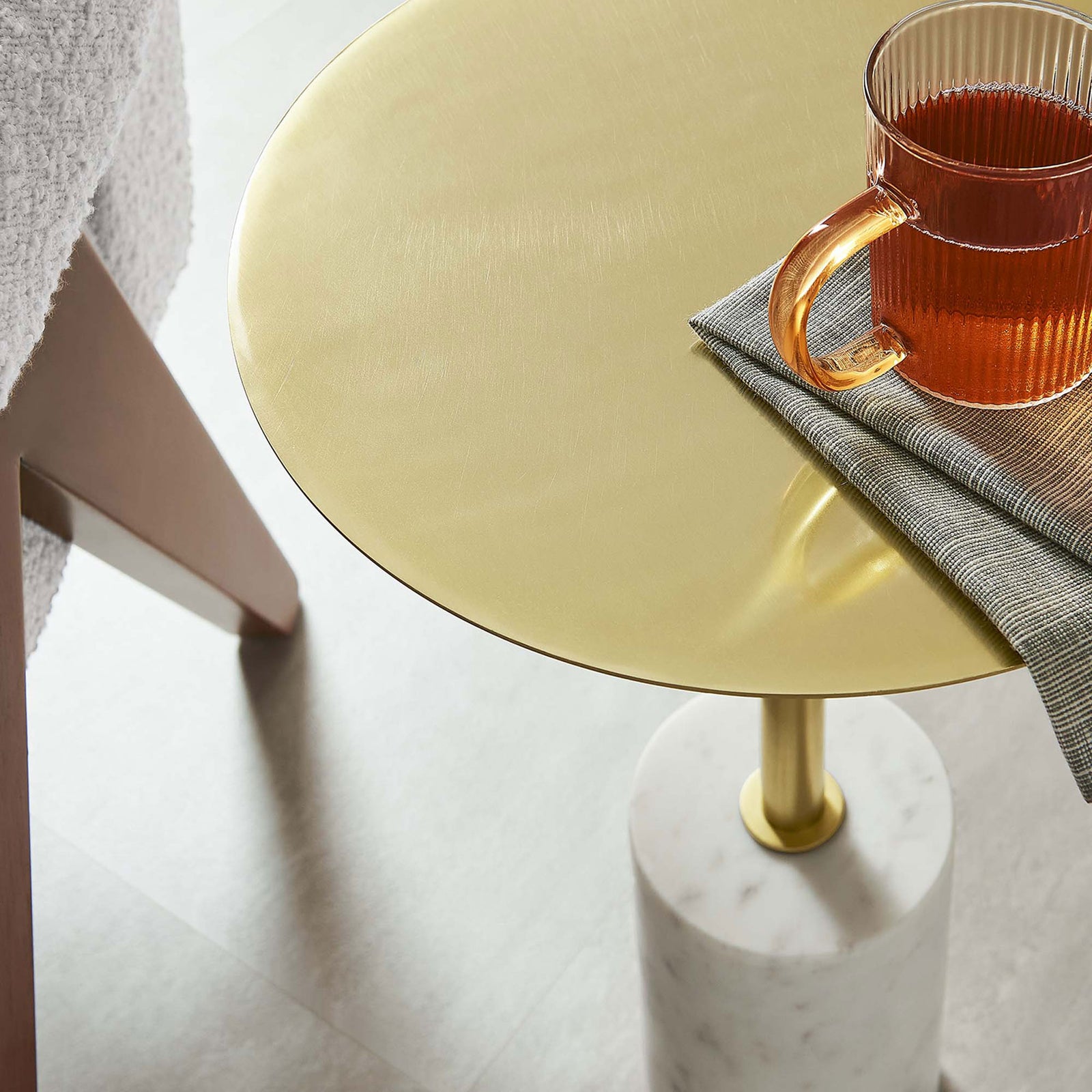 Brass side table holding a glass mug and napkin beside a cozy chair for everyday lounging || EEI-6605-WHI-BRA || detail_room