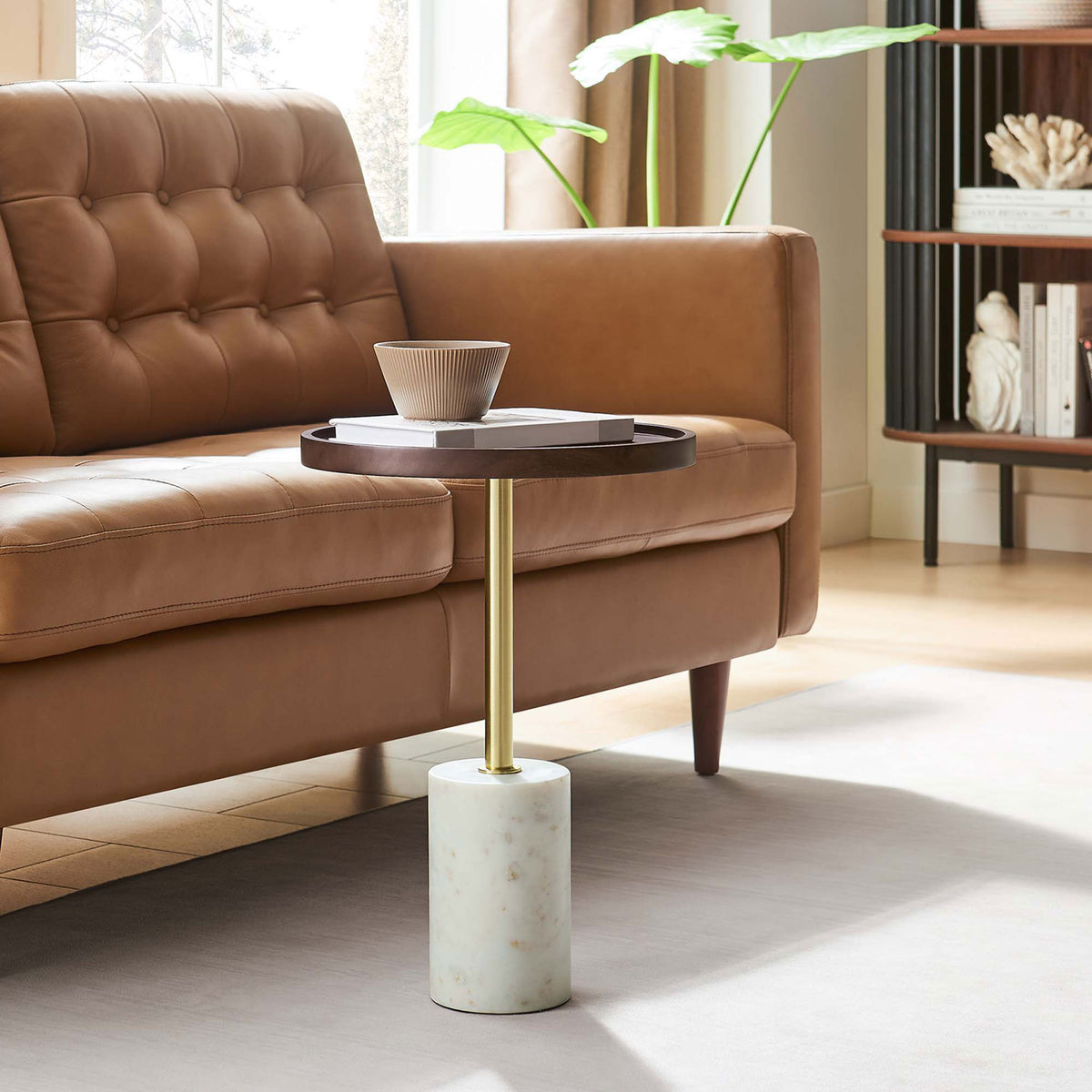 Round acacia and marble side table beside a tufted leather sofa in a bright living room. || EEI-6607-WHI-WAC || front_angle_room