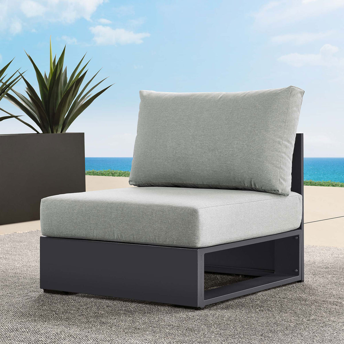 Light gray Tahoe outdoor armless chair arranged on a sunny patio with ocean backdrop and modern planter || EEI-6628-GRY-GRY || front_angle_room