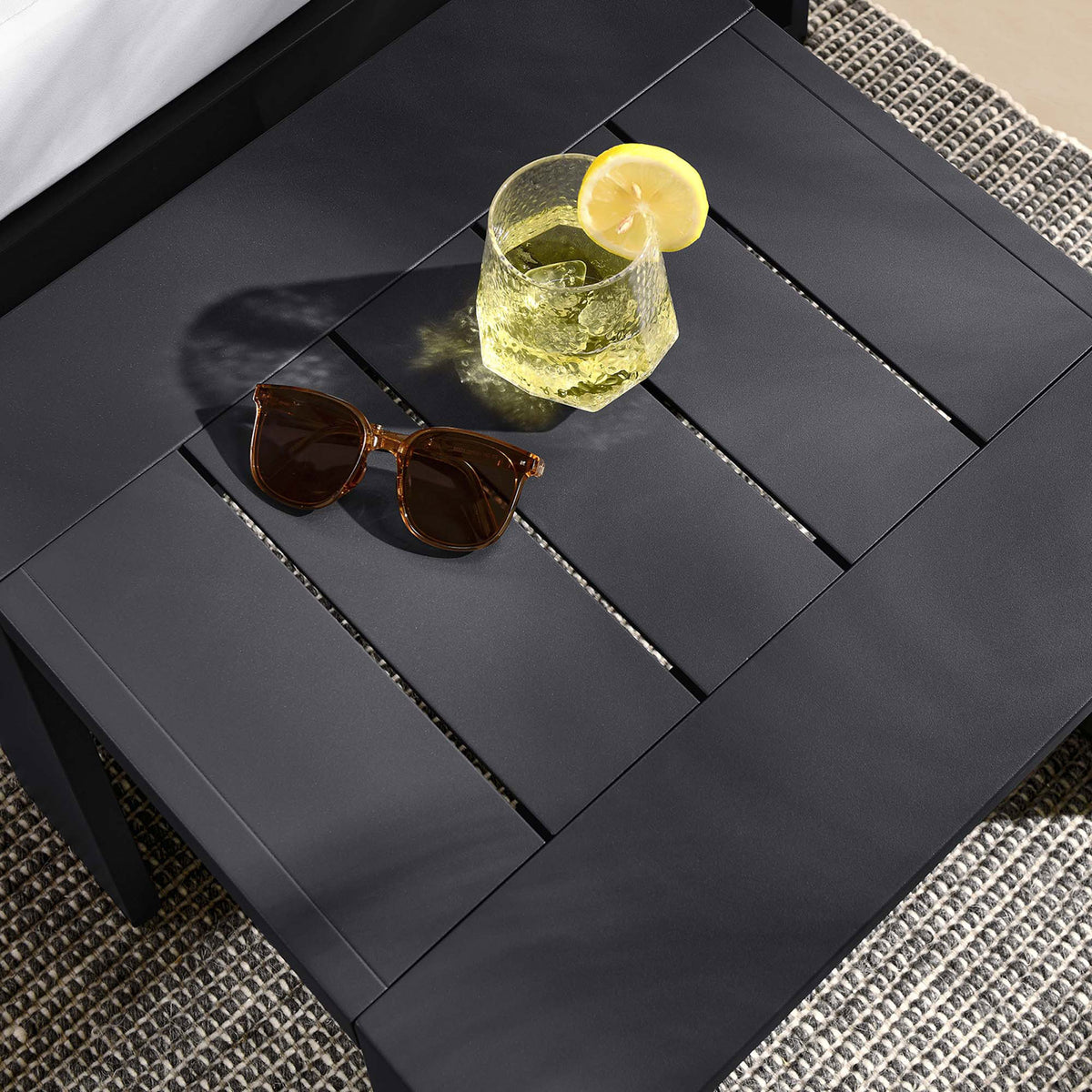 Slatted gray tabletop styled with a drink and sunglasses, adding modern texture to the outdoor seating area. || EEI-6635-GRY || detail_room