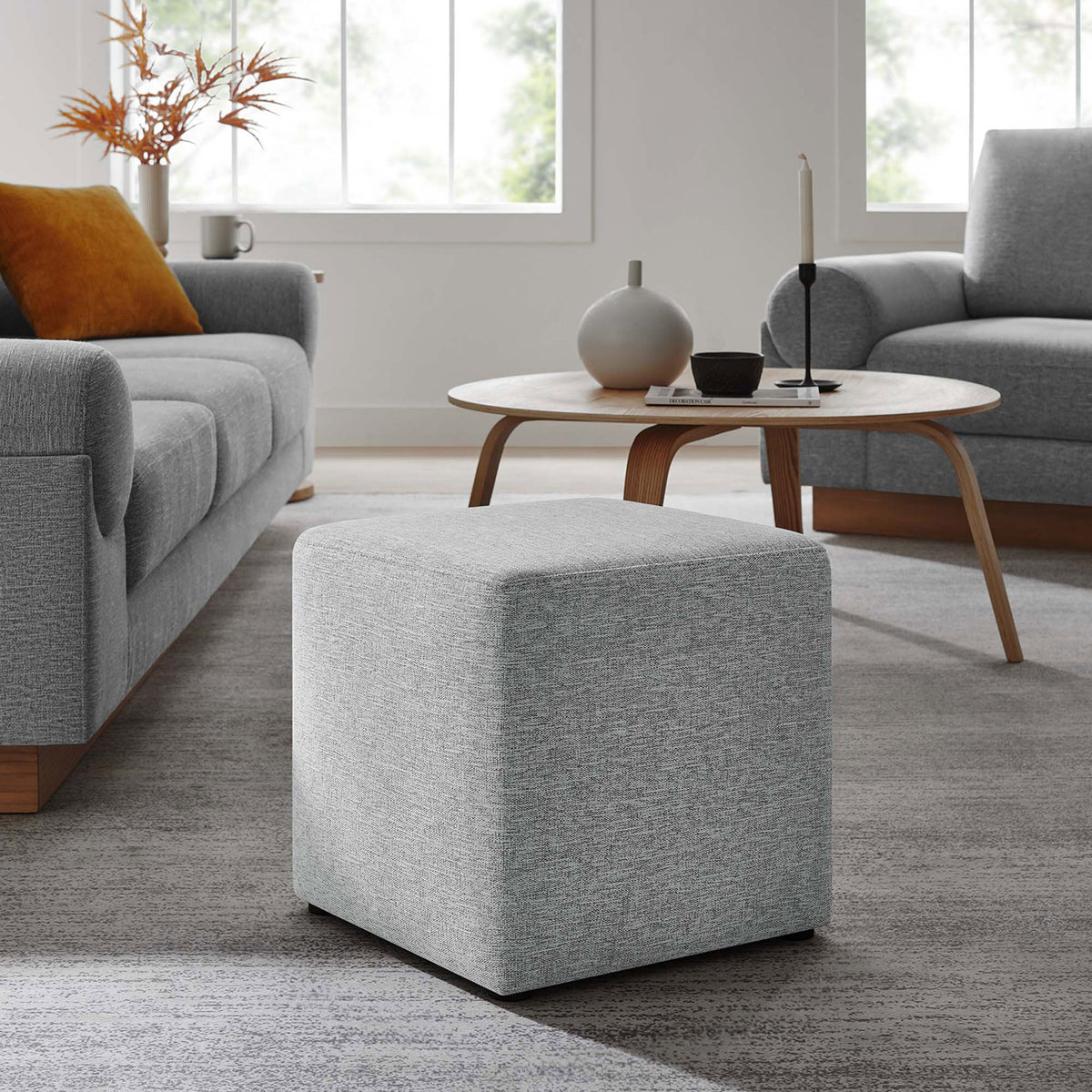 Light gray square ottoman centered in a cozy living room, complementing modern wood and fabric furniture || EEI-6636-HLG || front_angle_room
