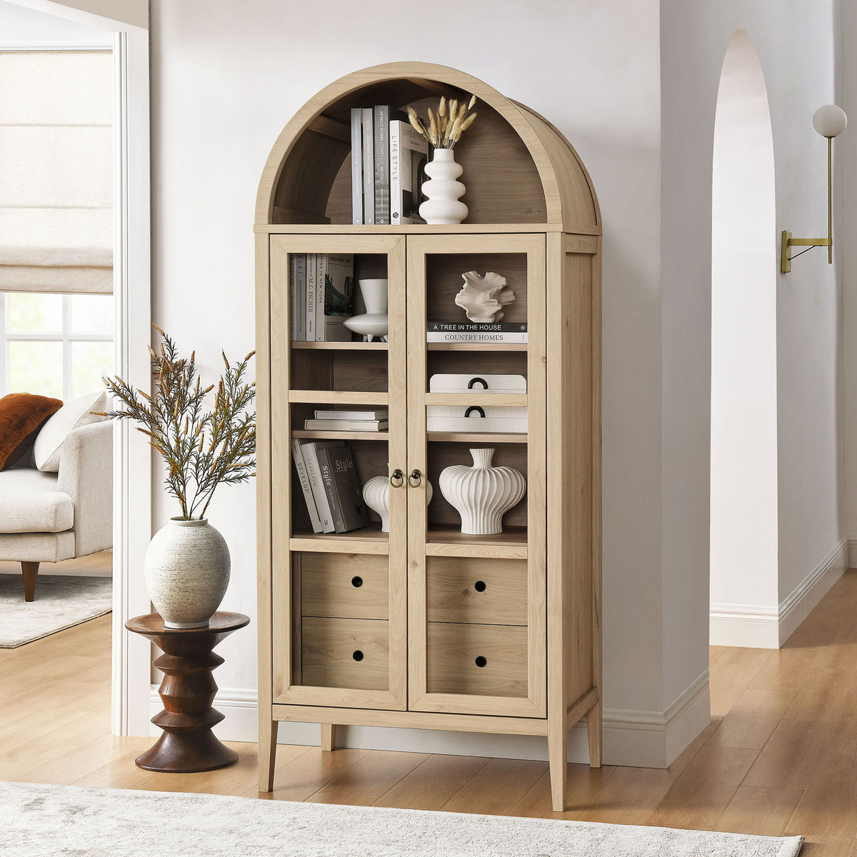 Light oak display cabinet filled with books and sculptural decor in a bright living space || EEI-6639-LOA || front_angle_room
