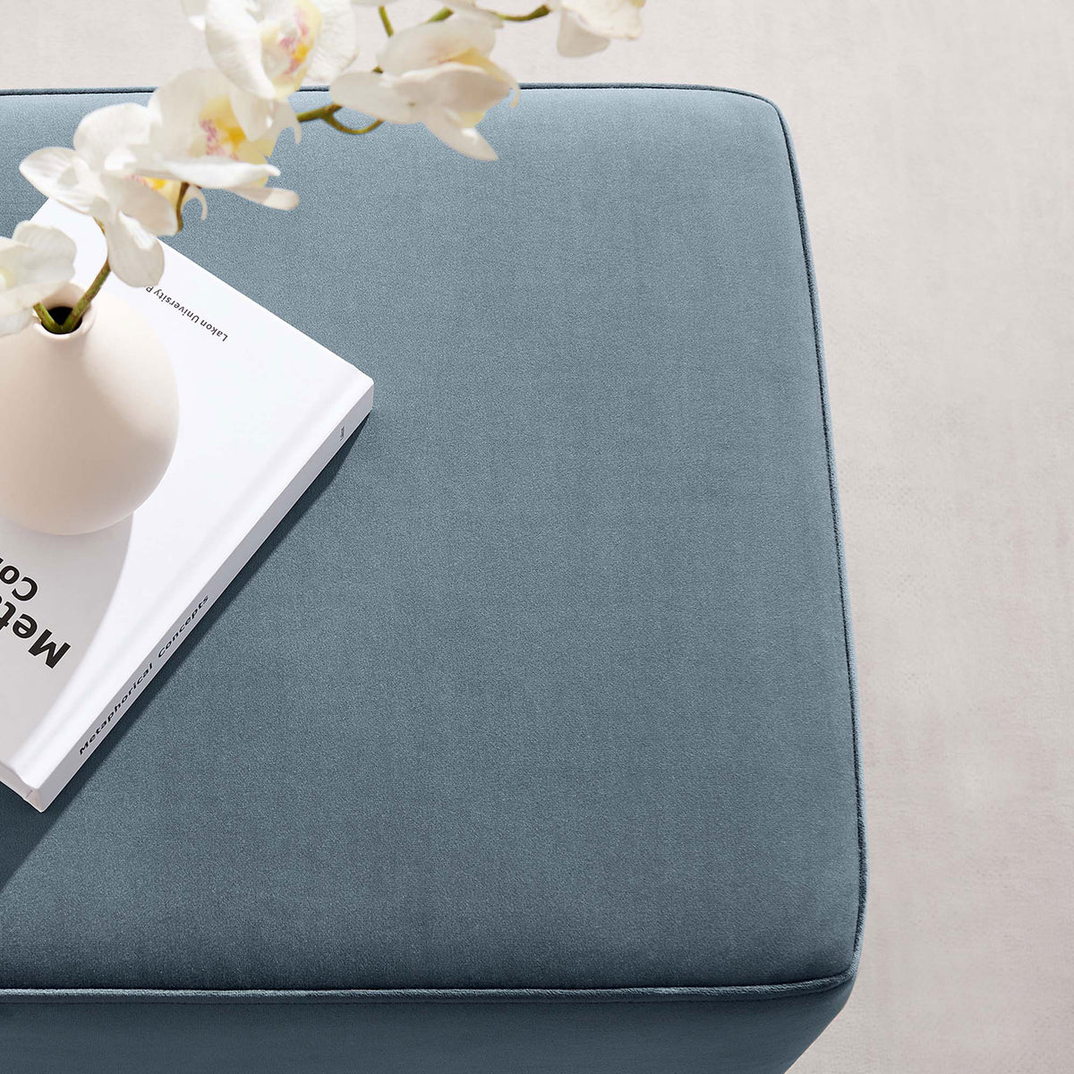 Styled cadet blue velvet ottoman doubles as a chic side table for books and decor accents. || EEI-6640-CAB-NAT || detail_room
