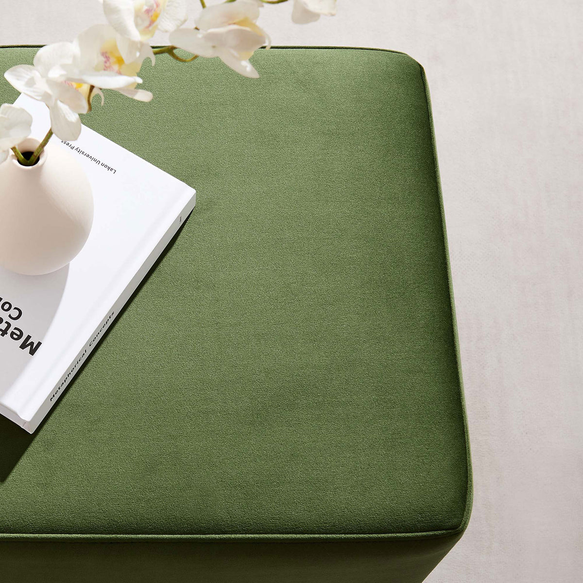 Top of moss green velvet ottoman styled with a book and floral vase || EEI-6640-MOG-NAT || detail_room