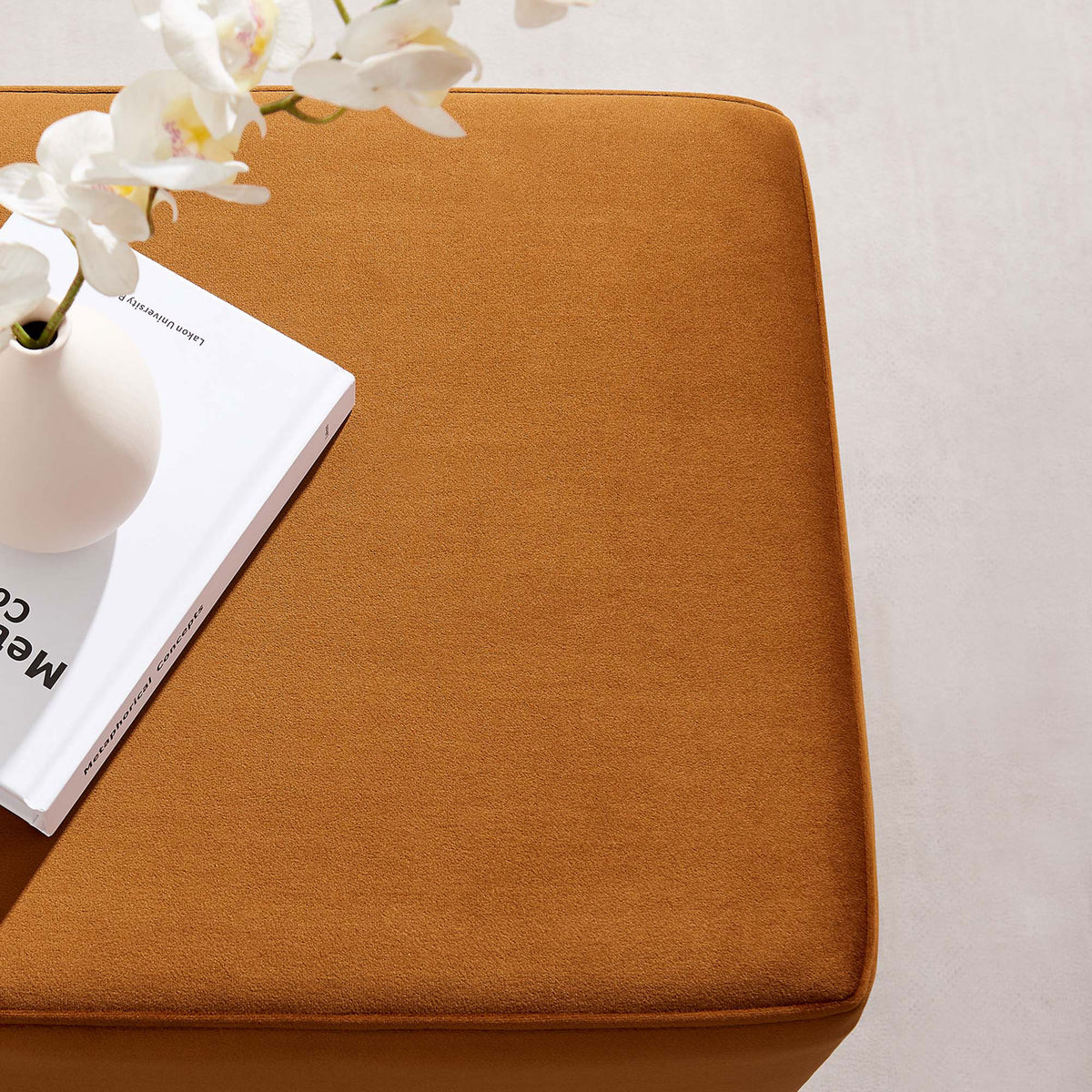 Rust velvet ottoman used as a side table with a vase and book in a bright modern space || EEI-6640-RUS-NAT || detail_room