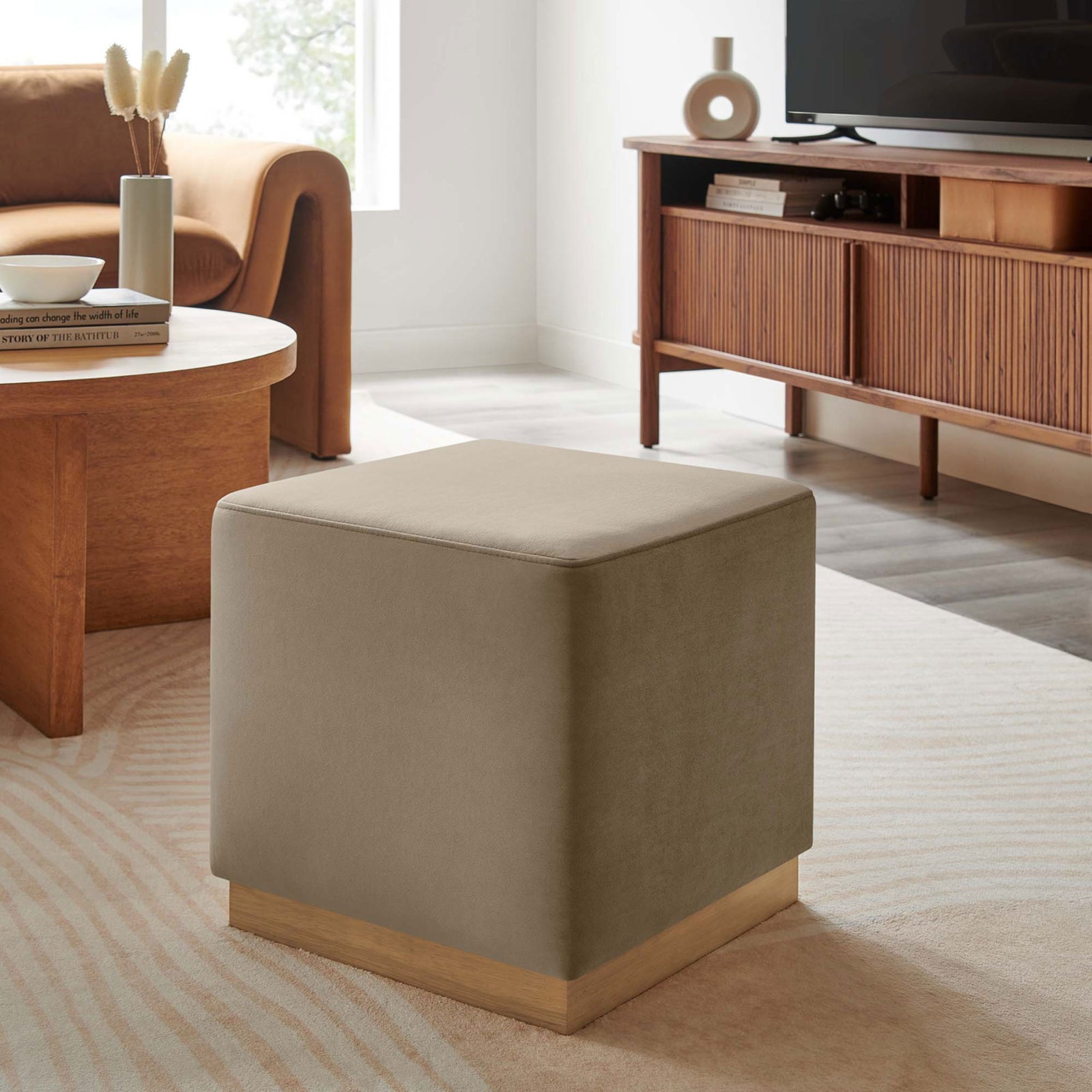 Neutral taupe ottoman pairs with warm wood furniture to complete a contemporary living room. || EEI-6640-TAU-NAT || front_angle_room
