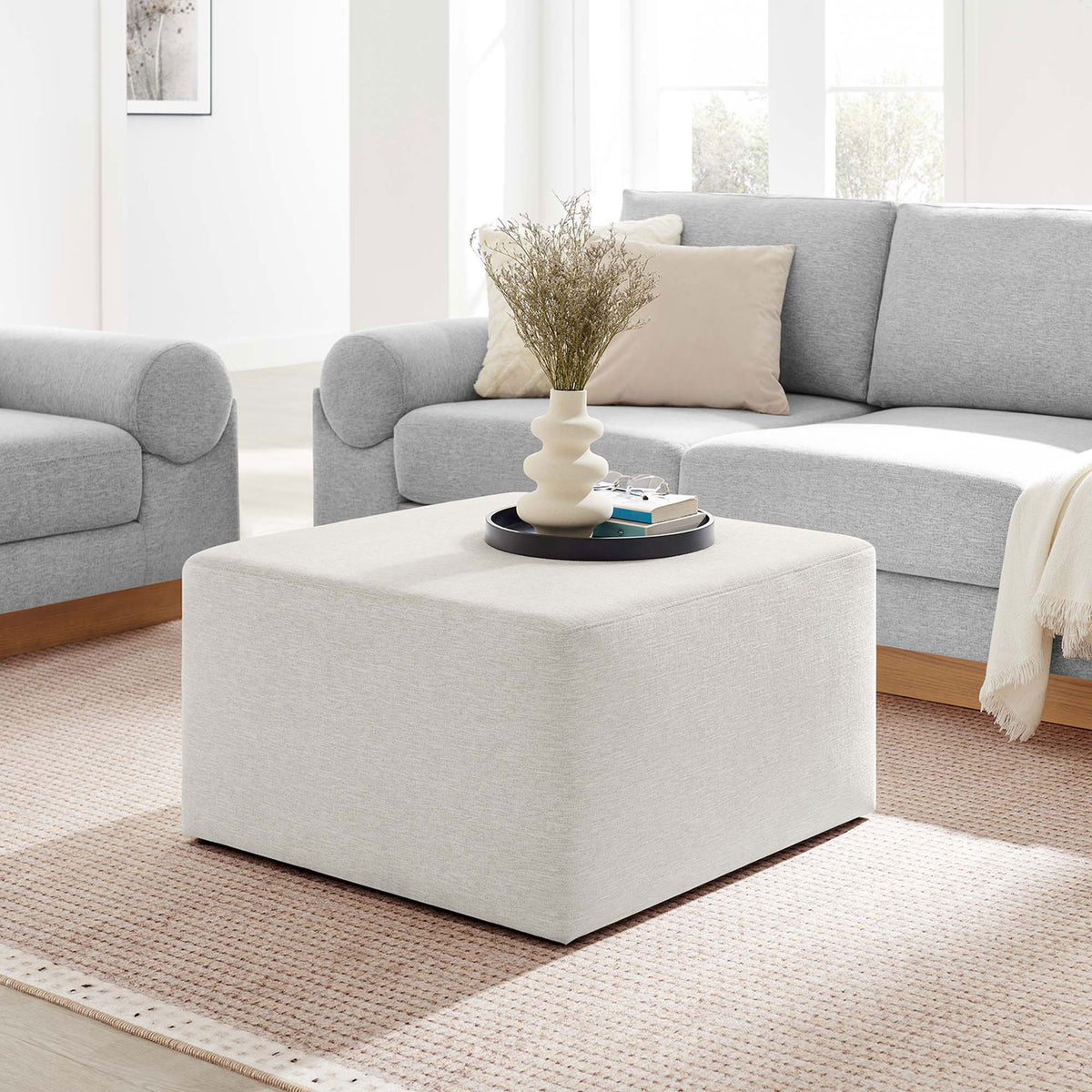 Large ivory ottoman anchors a bright living room, pairing effortlessly with cozy sofas and soft textiles || EEI-6642-HEI || front_angle_room