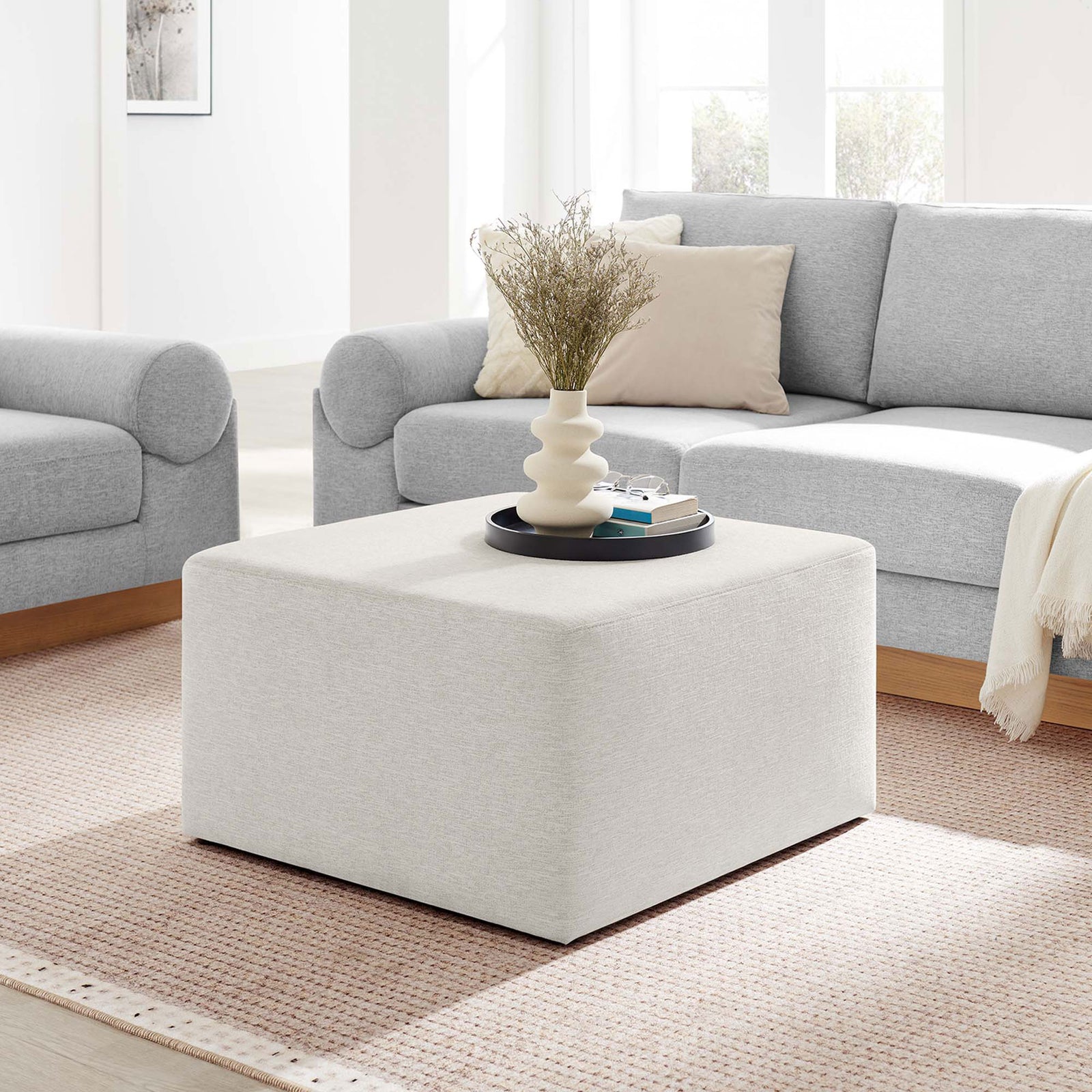 Large ivory ottoman anchors a bright living room, pairing effortlessly with cozy sofas and soft textiles || EEI-6642-HEI || front_angle_room