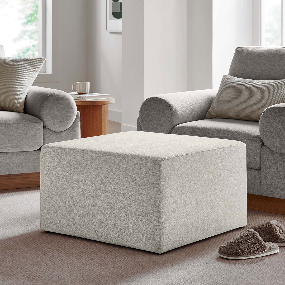 Plush ivory ottoman offers inviting extra seating between armchairs in a serene, softly lit living space || EEI-6642-HEI || front_angle_room