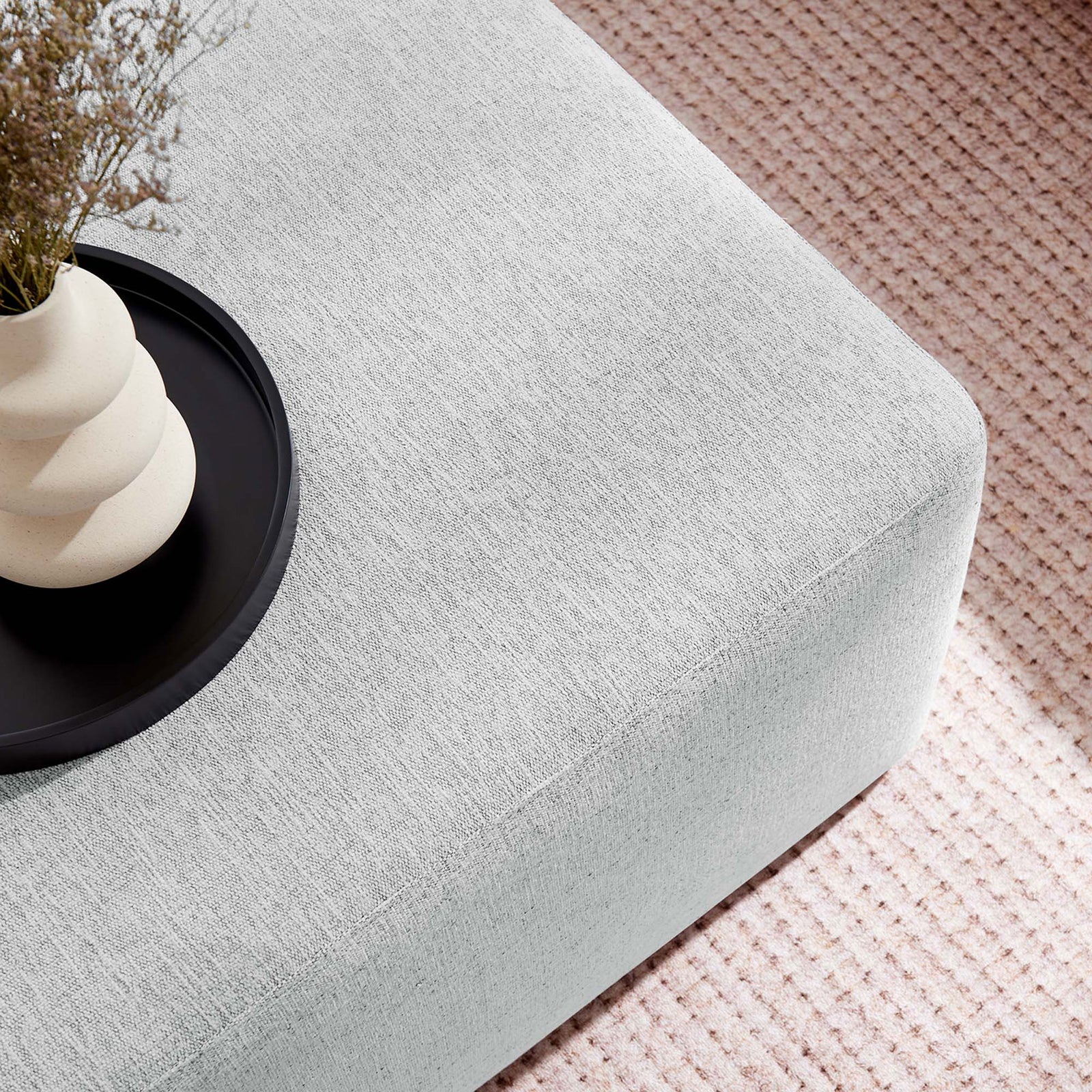 Light gray ottoman styled as a coffee table, topped with a black tray and sculptural vase over a textured rug || EEI-6642-HLG || detail_room