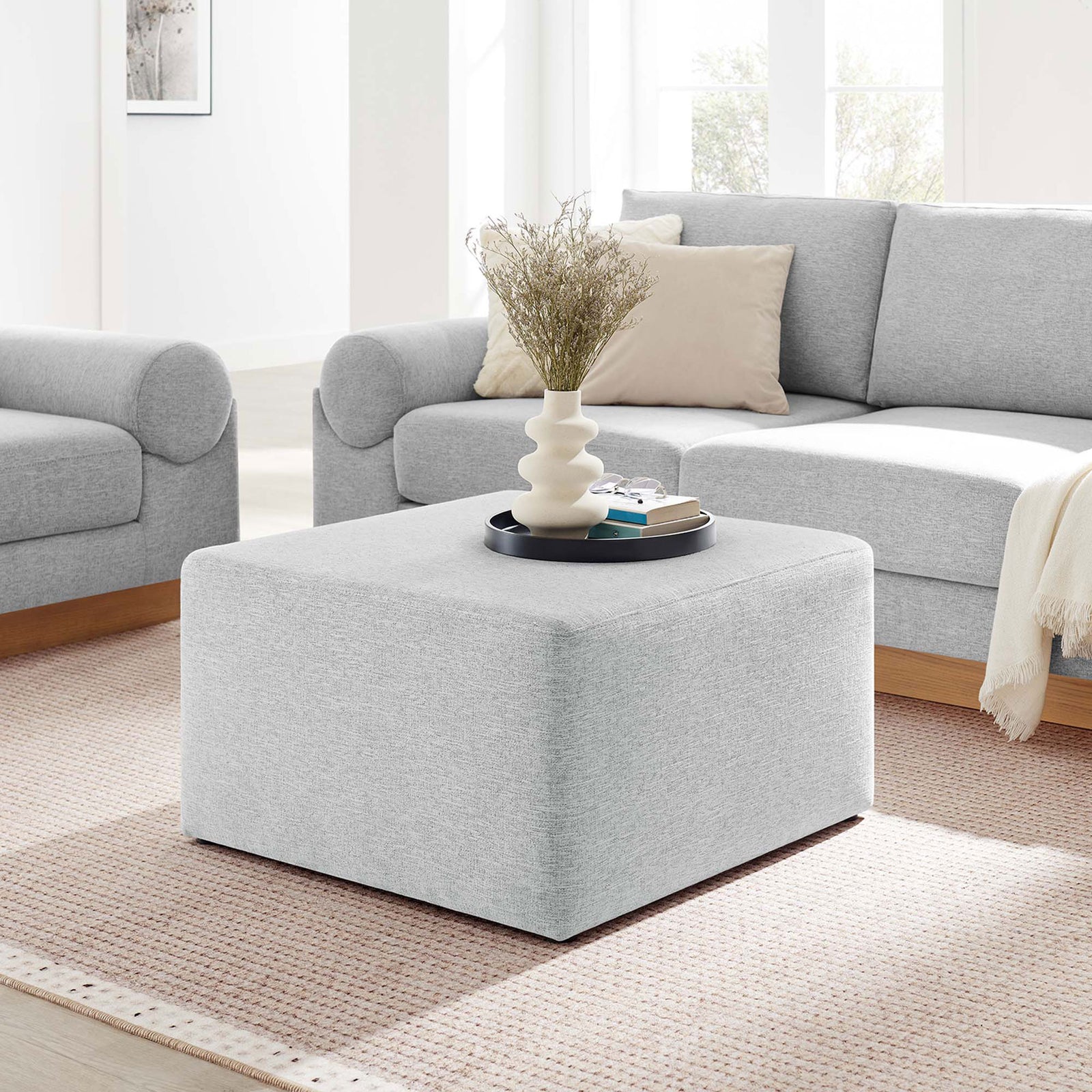 Light gray square ottoman anchoring a bright modern living room, paired with matching sofa and neutral decor || EEI-6642-HLG || front_angle_room