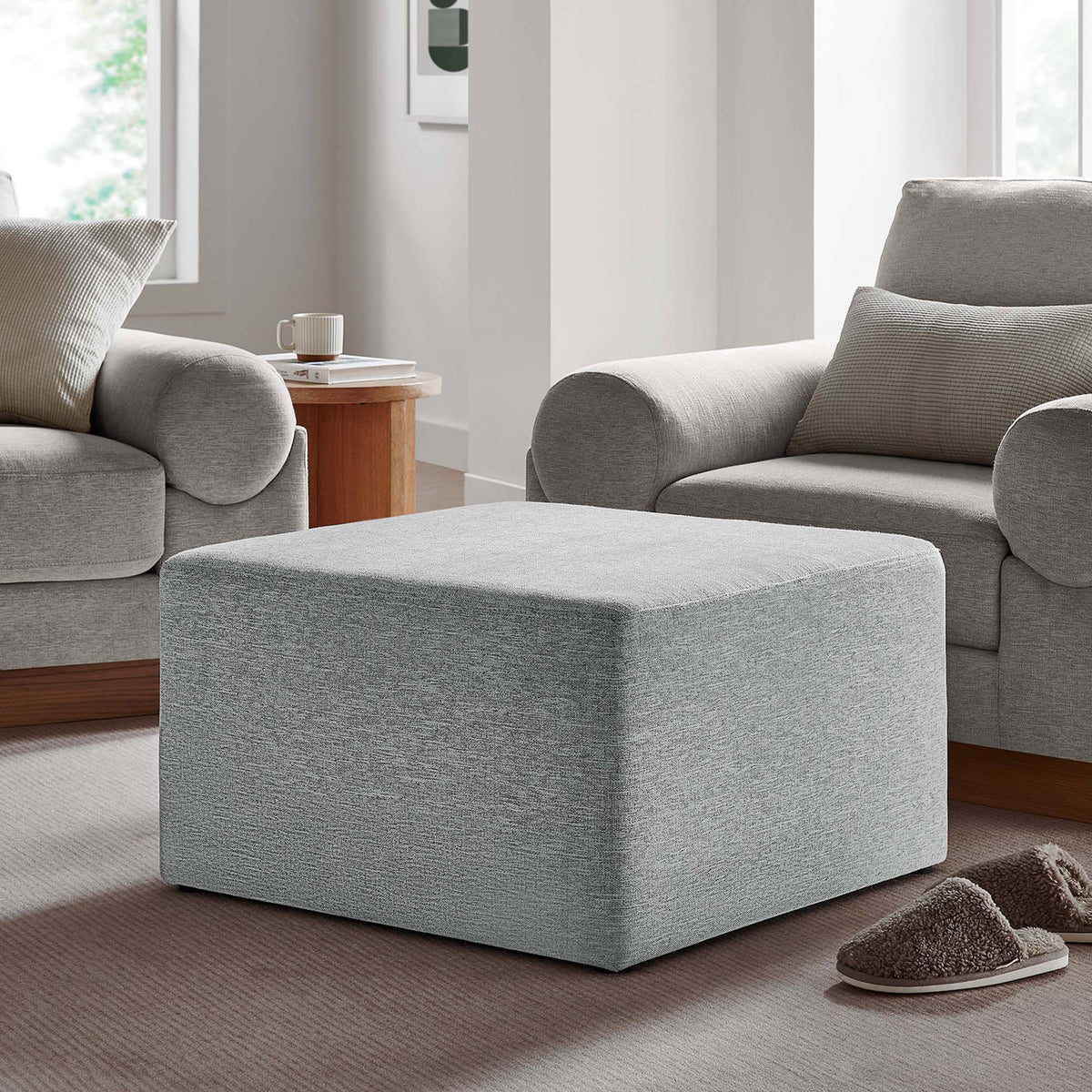 Light gray ottoman adding soft texture to a cozy living room, set between plush armchairs and warm wood accents || EEI-6642-HLG || front_angle_room