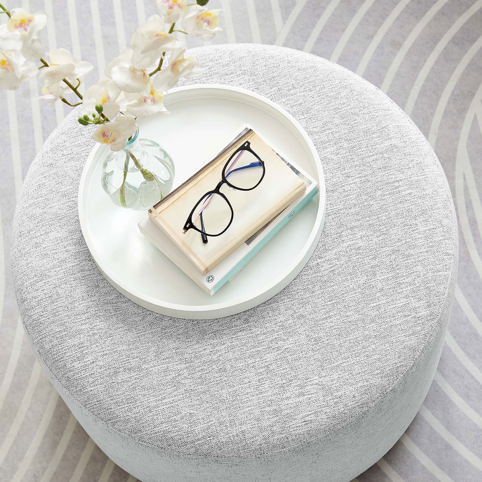 Round gray ottoman used as a chic coffee table with tray, flowers, and glasses in a modern living room || EEI-6645-HLG || top_room