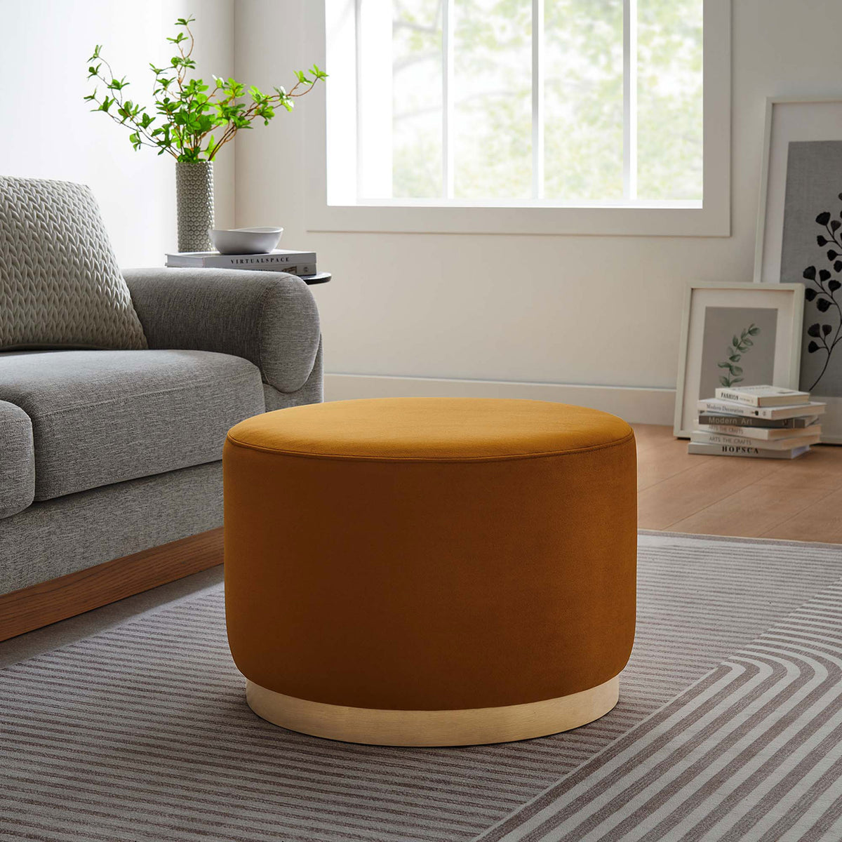 Round rust ottoman anchors a cozy seating nook, pairing warm velvet with a light wood base and soft rug || EEI-6646-RUS-NAT || front_room