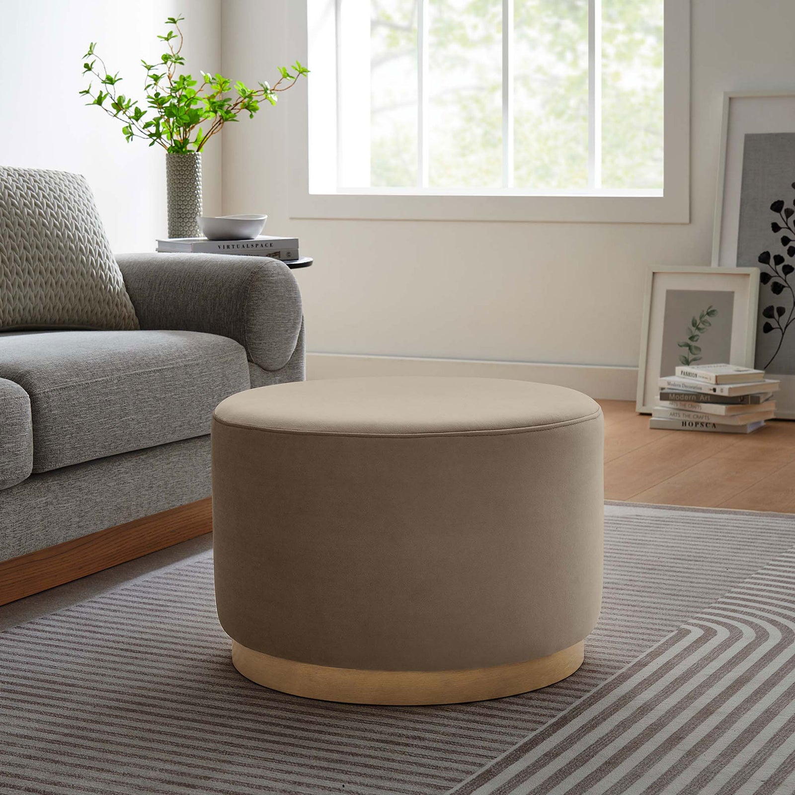 Round taupe ottoman beside a gray sofa, adding soft texture and extra seating to the living room || EEI-6646-TAU-NAT || front_angle_room