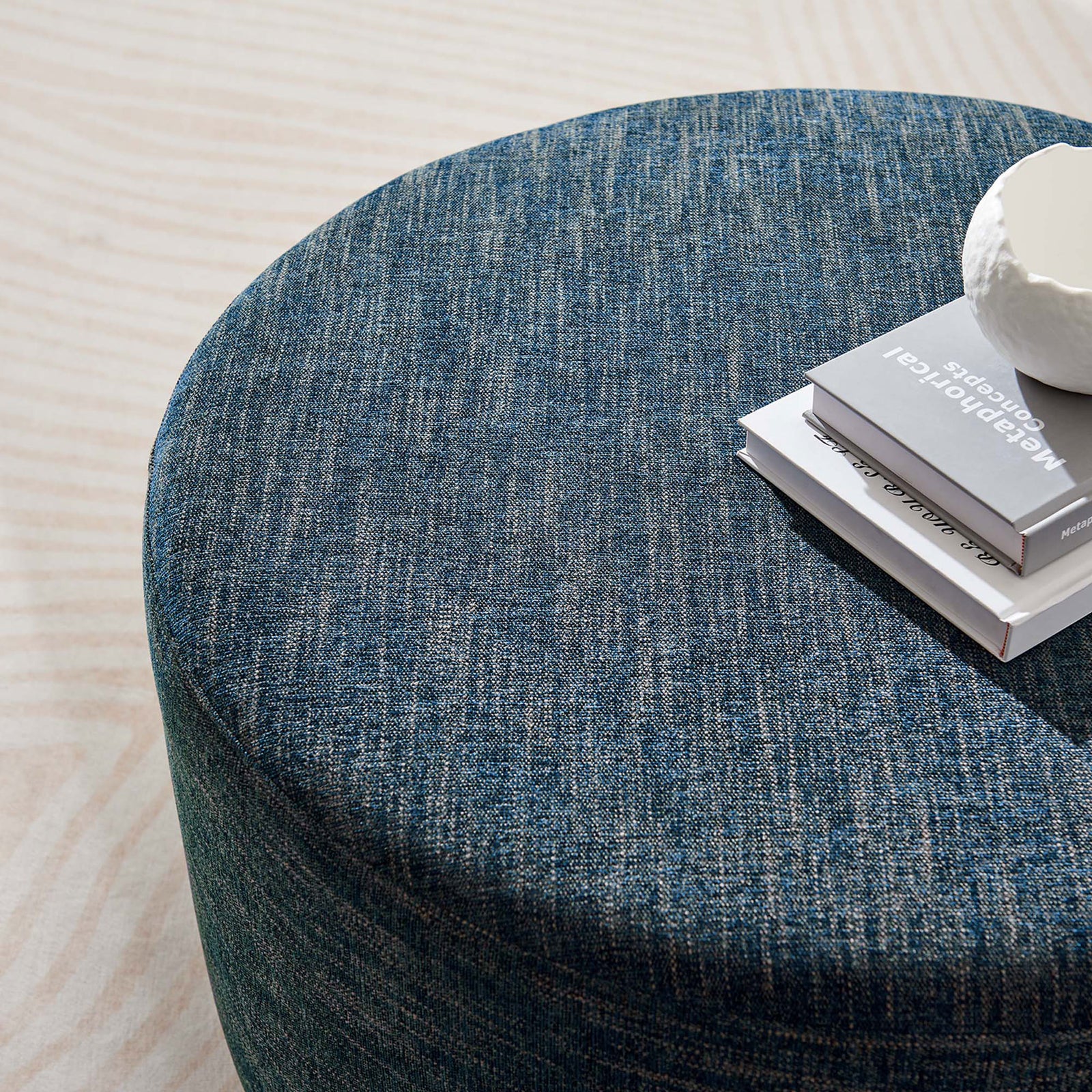 Cushioned top of the 29 inch round ottoman in heathered azure fabric serving as a casual tabletop || EEI-6647-HEA || top_angle_room