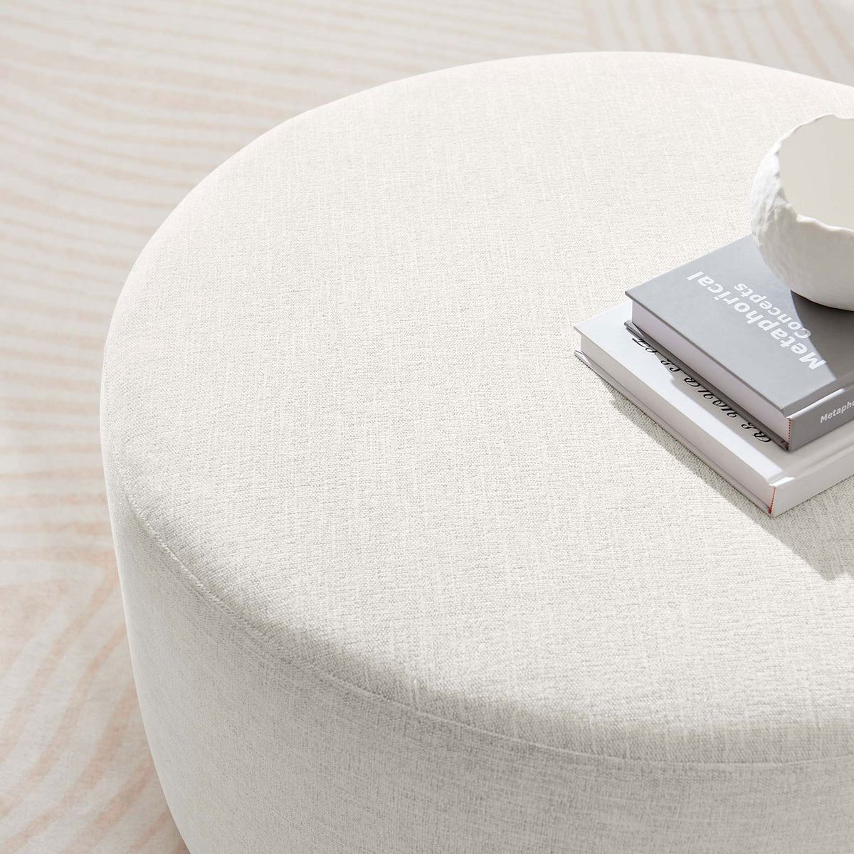 Textured ivory ottoman top doubles as a coffee table surface, styled with books and a sculptural bowl. || EEI-6647-HEI || detail_room
