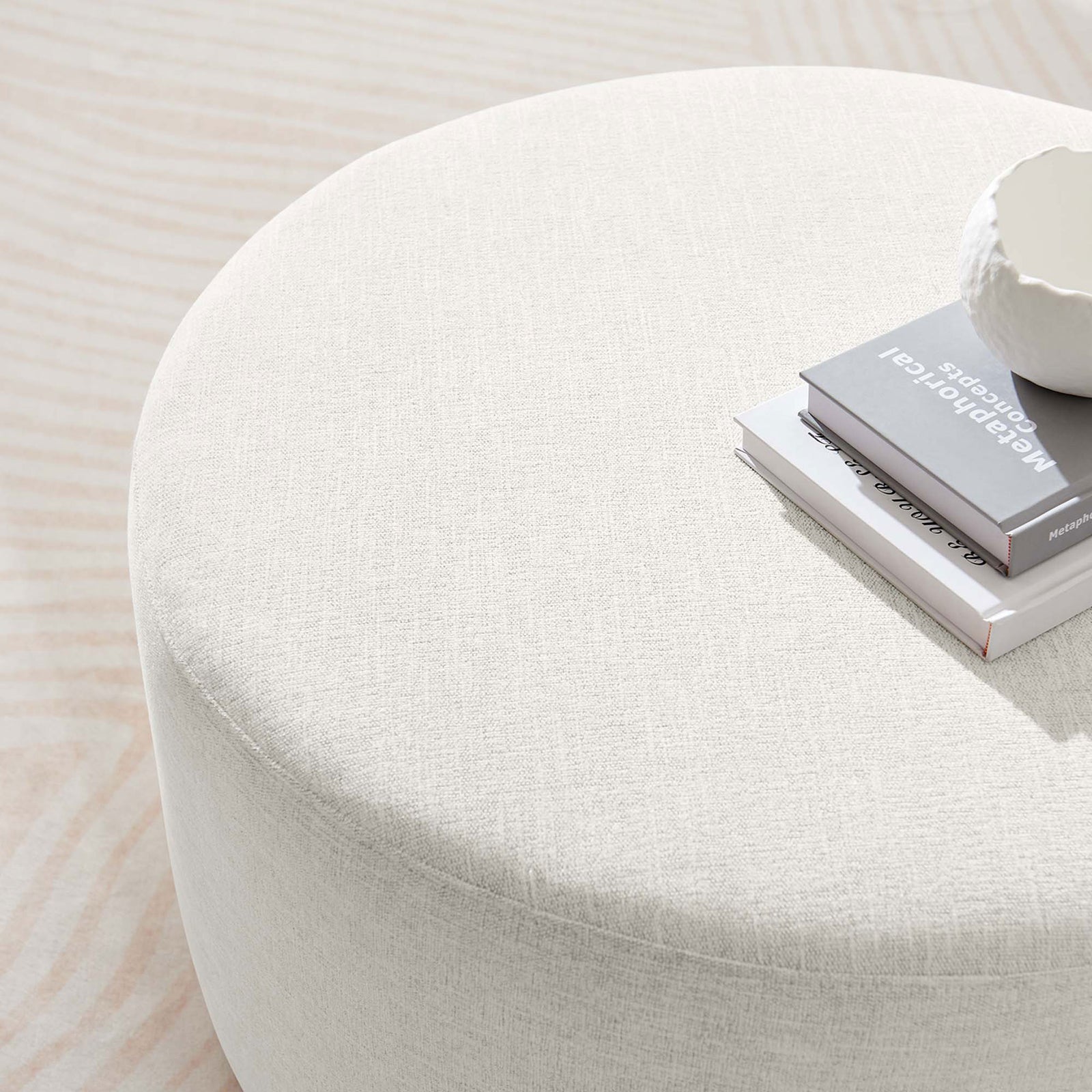 Textured ivory ottoman top doubles as a coffee table surface, styled with books and a sculptural bowl. || EEI-6647-HEI || detail_room