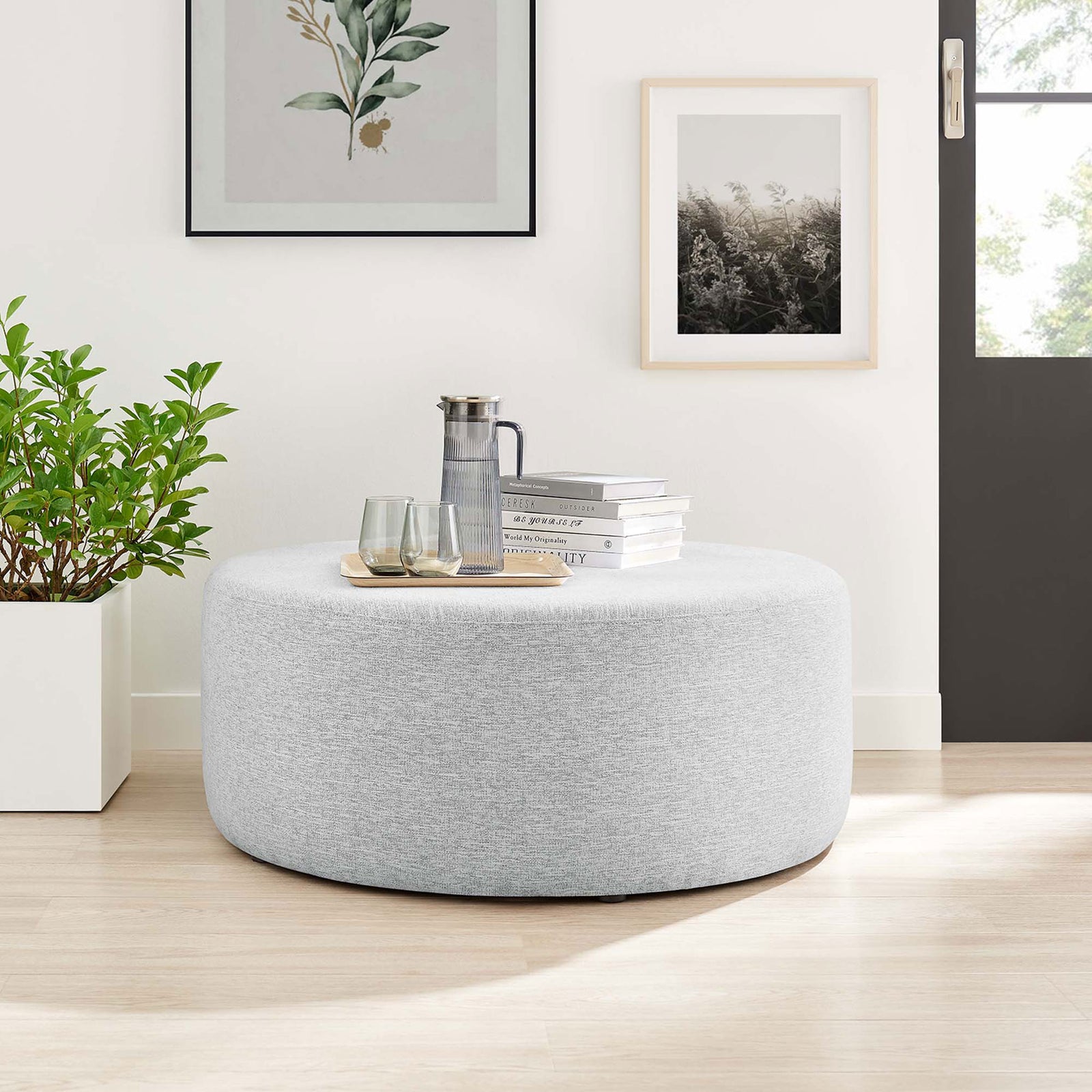 Spacious light gray round ottoman used as a coffee table in a modern living room with wood floors || EEI-6649-HLG || front_room