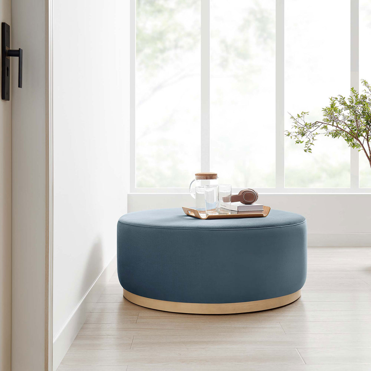 Large cadet blue round ottoman with natural base styled in a bright room beside a window and tray || EEI-6650-CAB-NAT || front_room