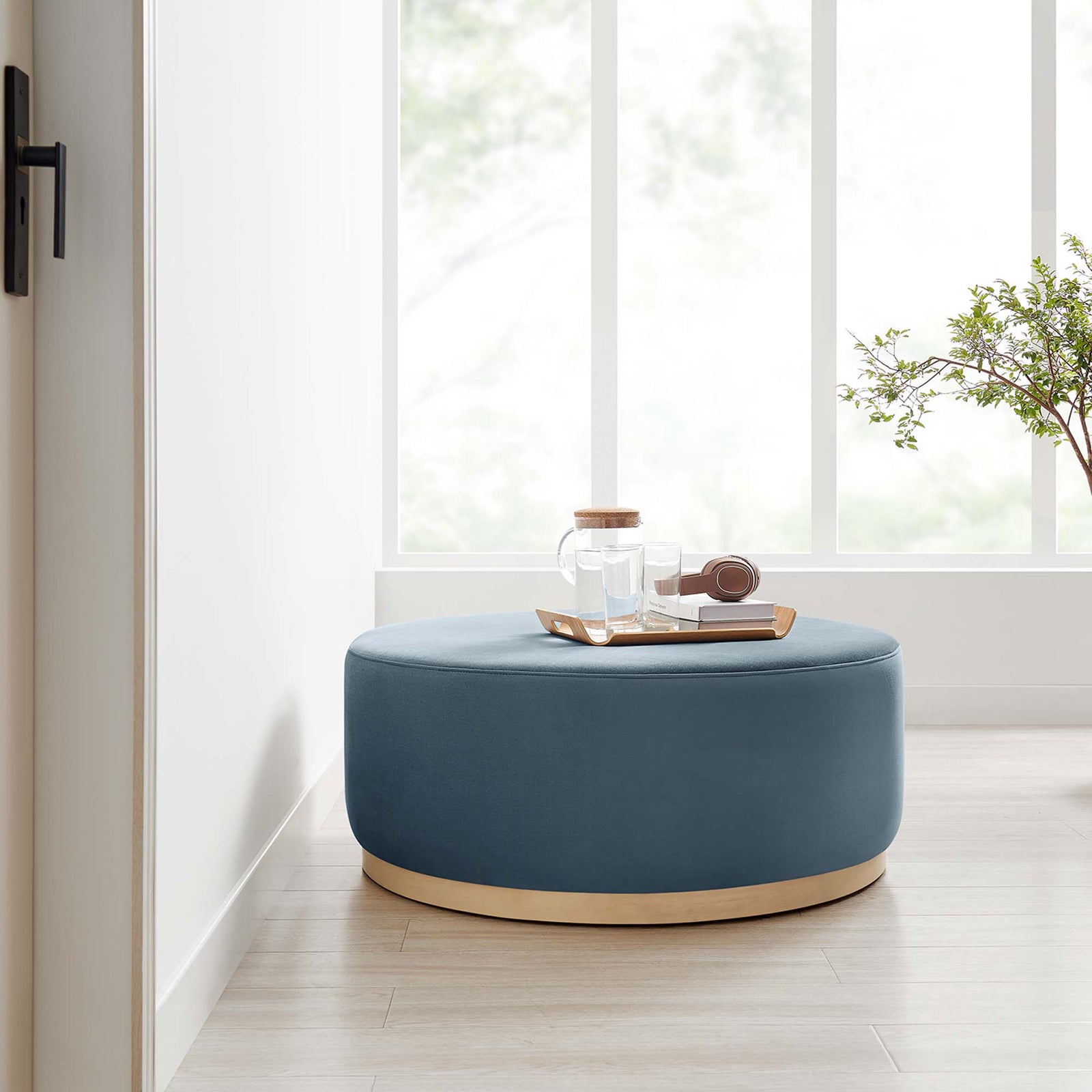 Large cadet blue round ottoman with natural base styled in a bright room beside a window and tray || EEI-6650-CAB-NAT || front_room
