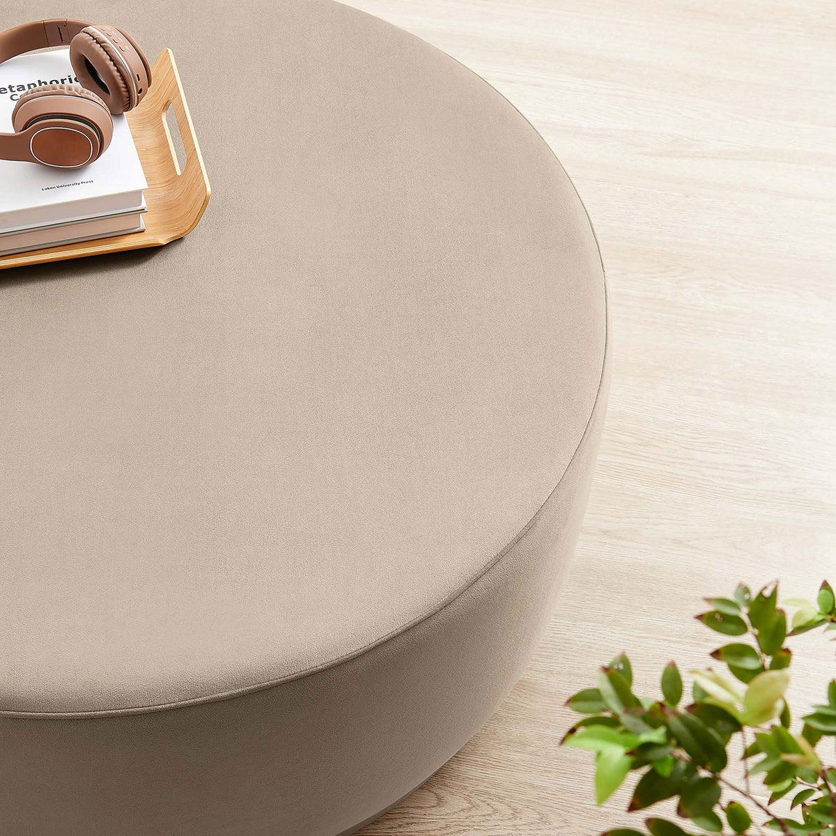 Large taupe round ottoman topped with tray, headphones, and decor on a light wood floor || EEI-6650-TAU-NAT || detail_room