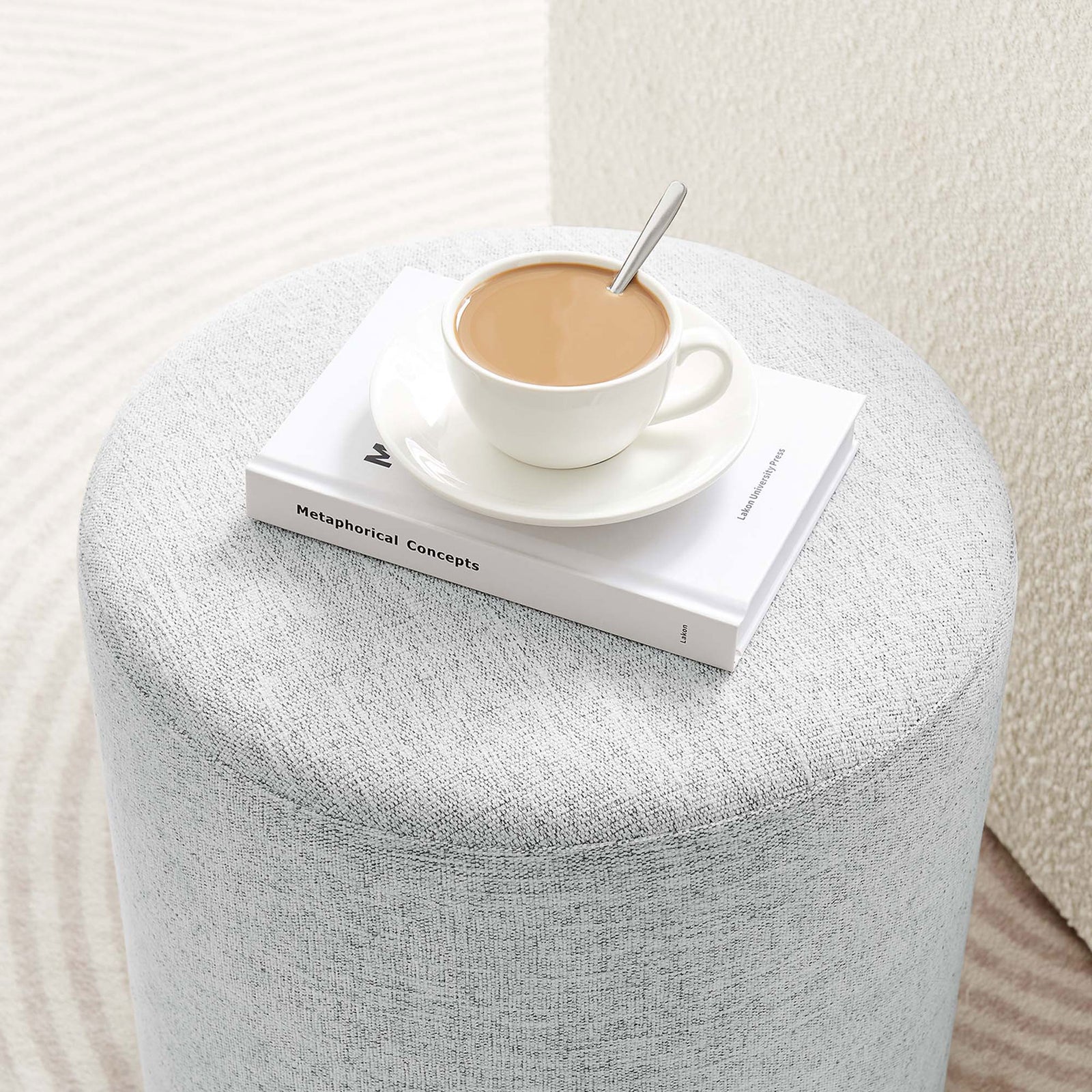 Ottoman styled as a small side table holding a coffee cup and book in a bright room || EEI-6651-HLG || detail_room