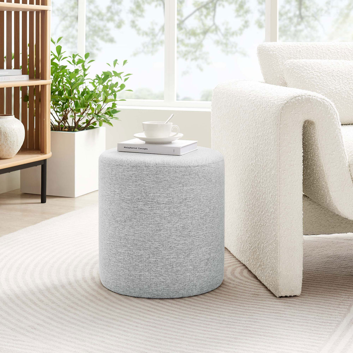 Light gray round ottoman beside a modern white accent chair in a sunlit living room || EEI-6651-HLG || front_room