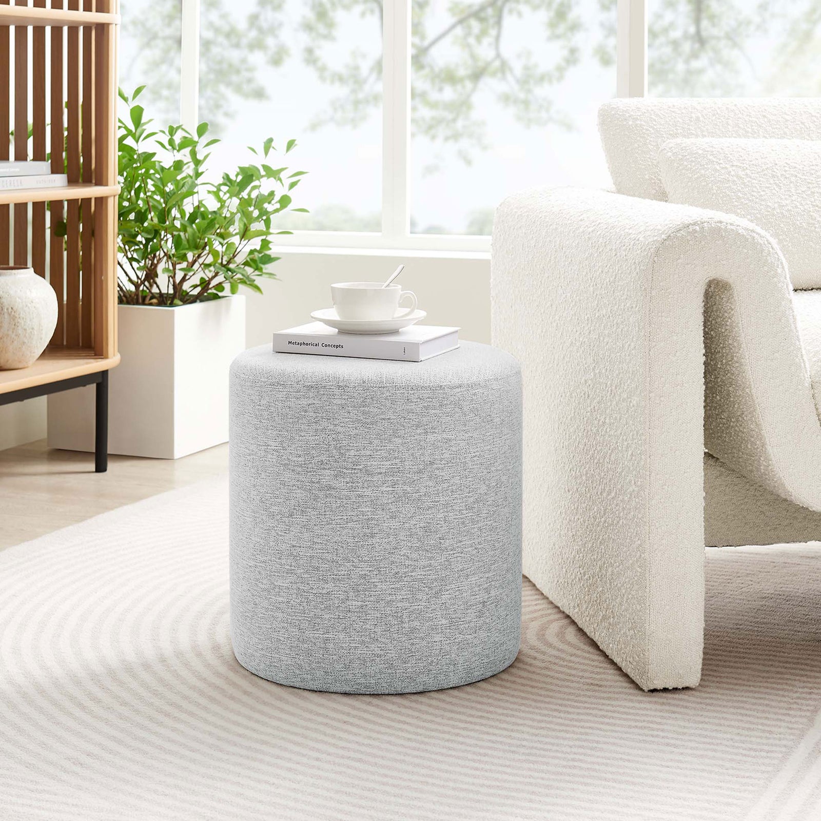 Light gray round ottoman beside a modern white accent chair in a sunlit living room || EEI-6651-HLG || front_room