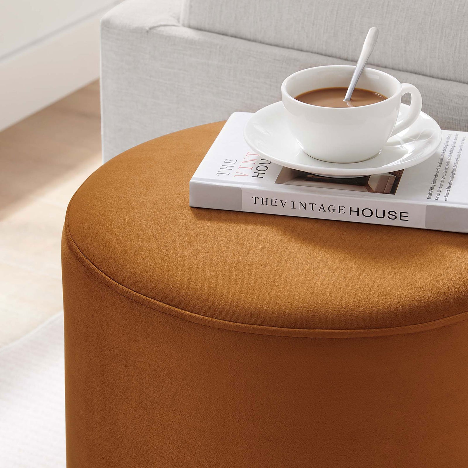 Rust velvet ottoman doubles as a small side table, holding coffee and books beside a cozy upholstered sofa || EEI-6652-RUS-NAT || detail_room