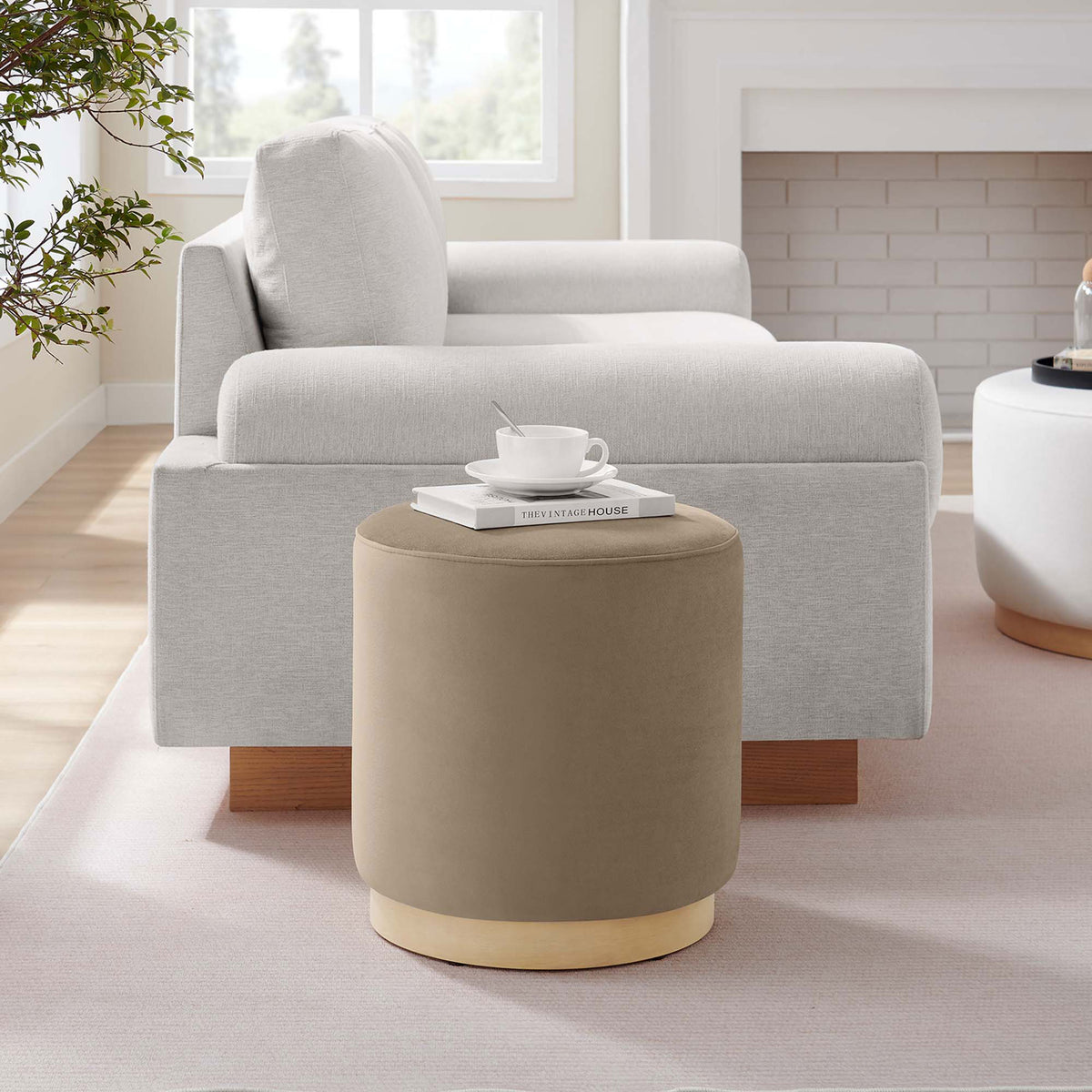 Taupe round ottoman styled next to a modern sofa as a versatile accent seat or side table || EEI-6652-TAU-NAT || front_angle_room