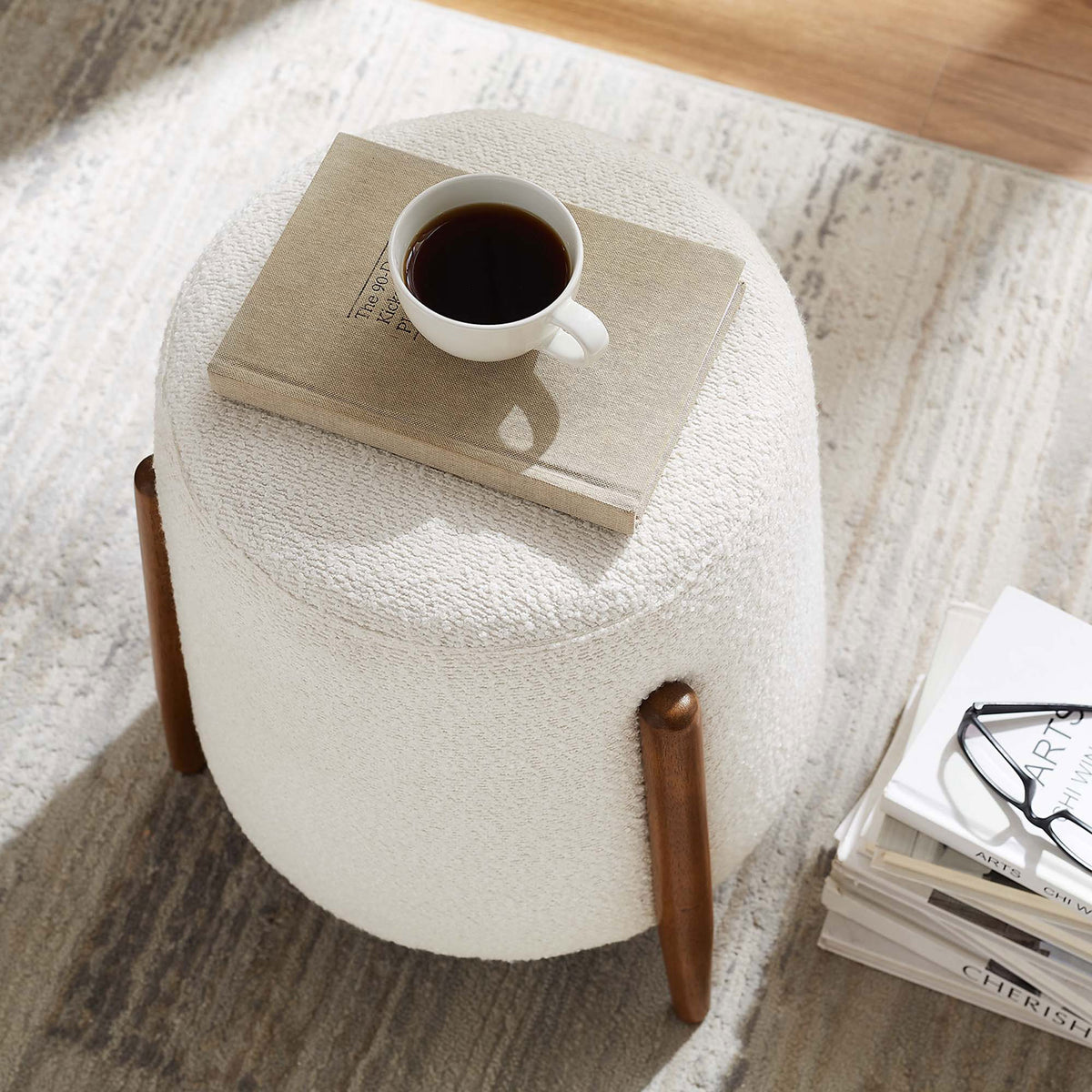 Boucle ottoman doubles as a petite coffee perch beside books on a soft neutral rug || EEI-6686-CLO || top_angle_room