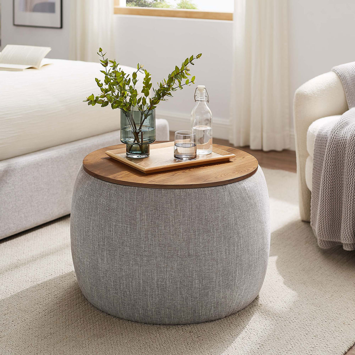 Round storage ottoman used as a bedside table, topped with tray, bottle, and greenery || EEI-6688-HEW || front_angle_room