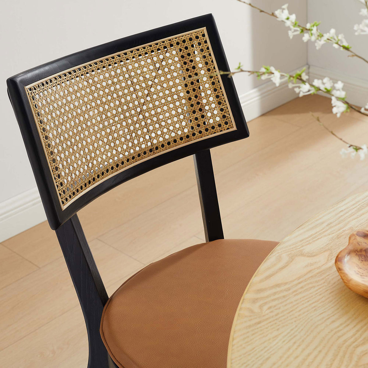 Rattan back black wood dining chair with tan vegan leather seat beside a light wood dining table || EEI-6732-BLK-TAN || detail_room