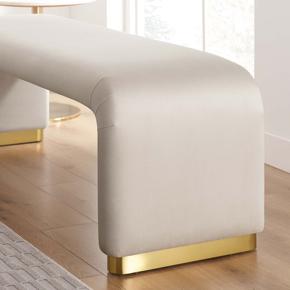 Rounded end and brass base glow in a cozy room scene, highlighting the plush almond velvet finish || EEI-6734-BRA-ALM || leg_room