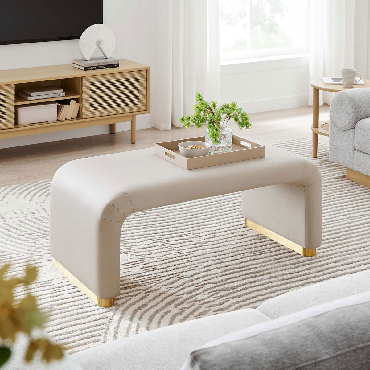 Modern room featuring the Koda waterfall ottoman in almond velvet paired with a striped rug and media console || EEI-6735-BRA-ALM || front_angle_room