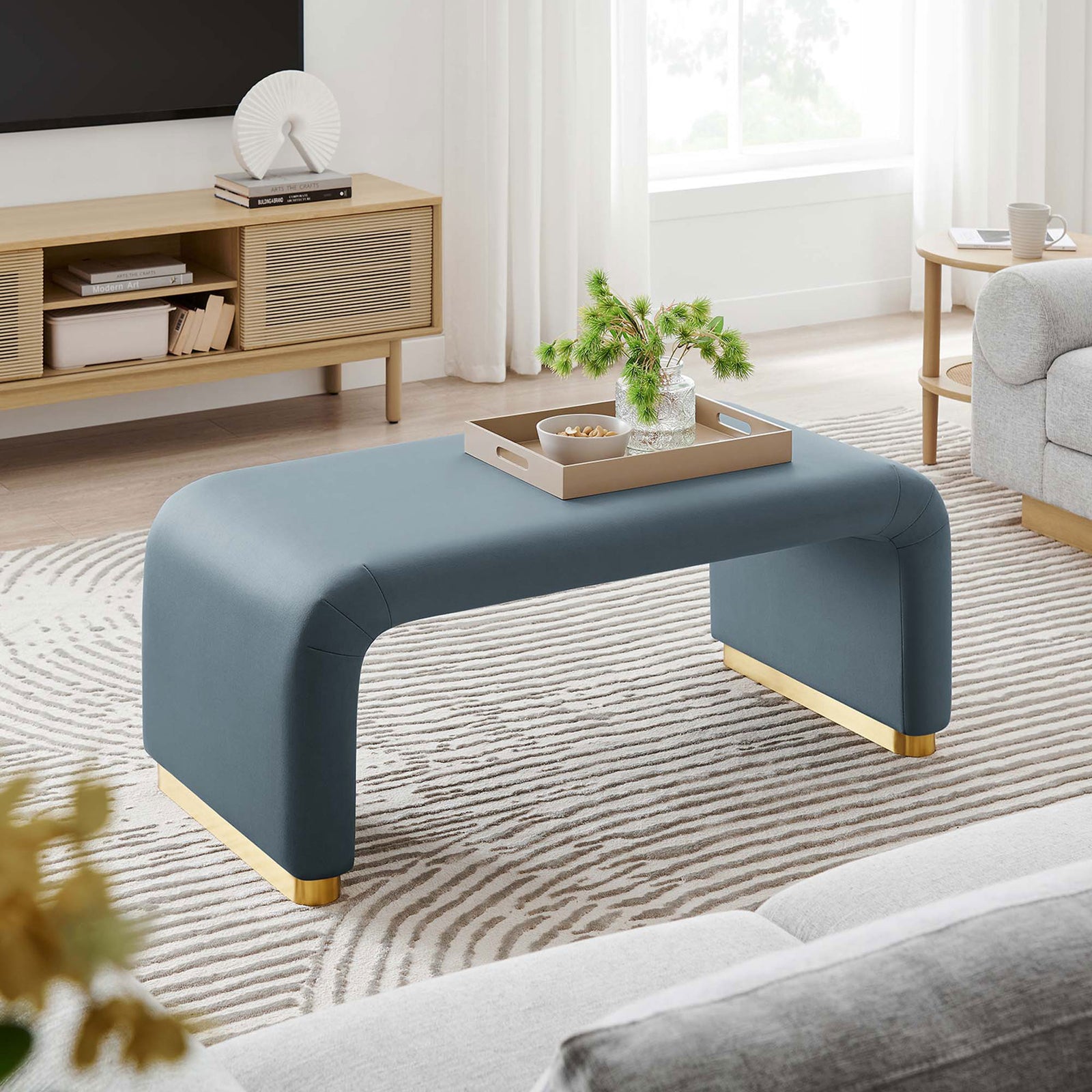 Waterfall ottoman anchors a modern living room, pairing plush performance velvet with a gleaming brass base. || EEI-6735-BRA-CAB || front_angle_room