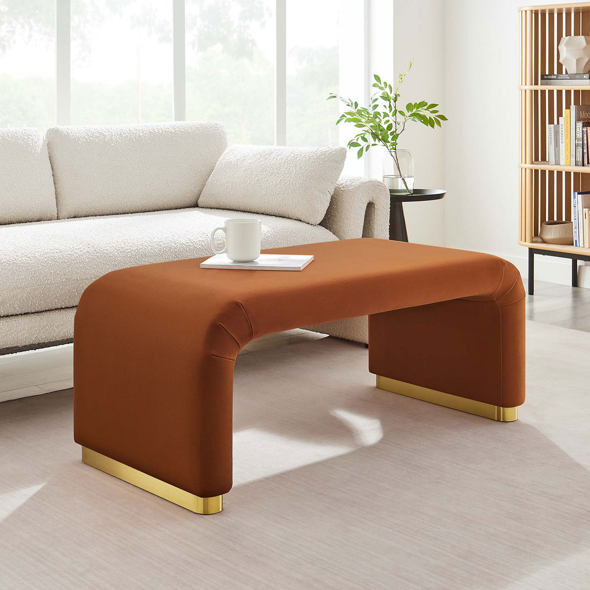 Brass rust velvet waterfall ottoman anchoring a bright lounge with curved sofa and minimalist decor || EEI-6735-BRA-RUS || front_angle_room