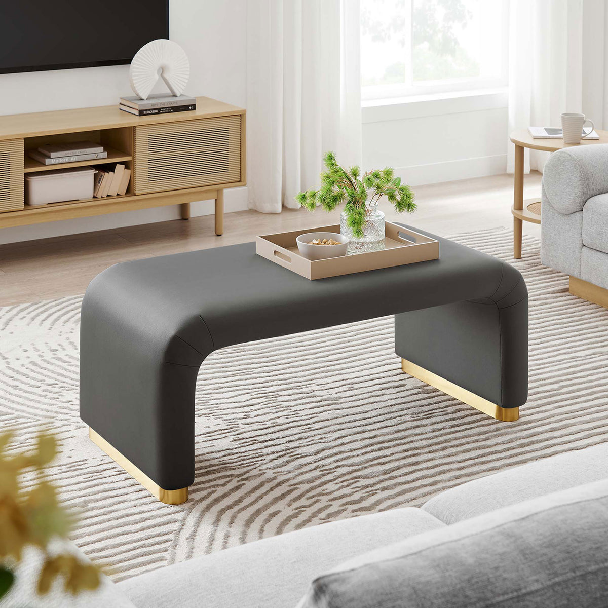 Storm gray waterfall ottoman styled as a coffee table in a bright modern living room with soft neutral furnishings || EEI-6735-BRA-STG || front_angle_room