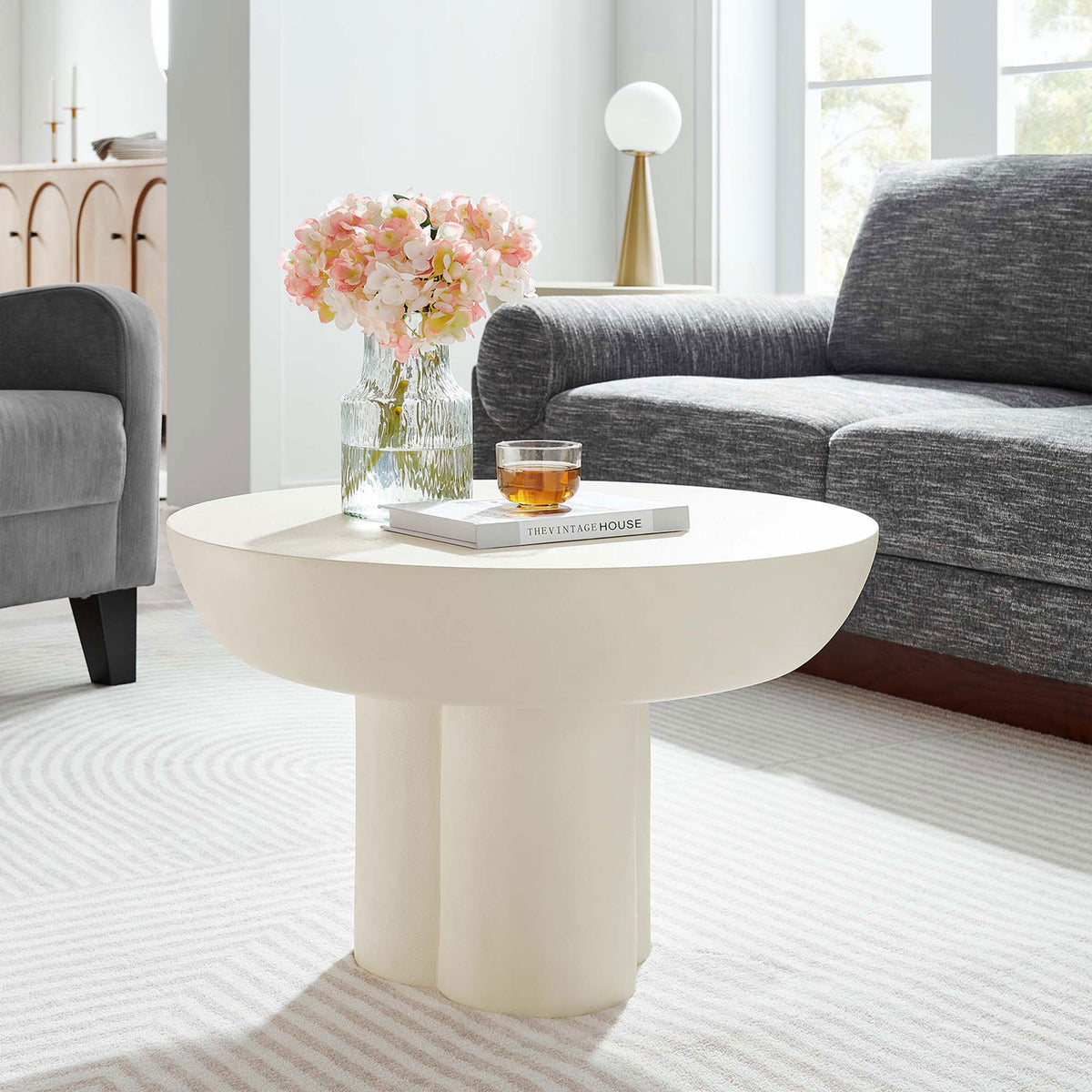 A sculptural white round coffee table adds modern character to a cozy living room setting || EEI-6760-WHI || front_angle_room