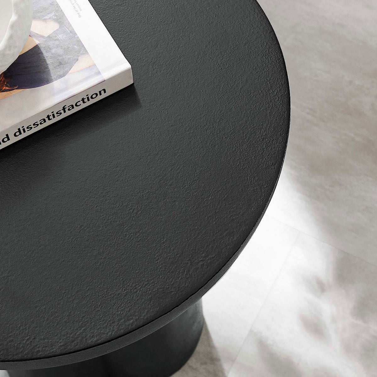 Styled view of the black concrete overlay side table top beside a book, adding modern texture to the living room || EEI-6761-BLK || detail_room