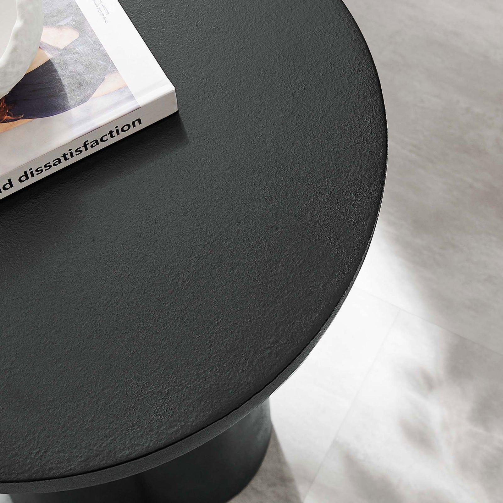 Styled view of the black concrete overlay side table top beside a book, adding modern texture to the living room || EEI-6761-BLK || detail_room