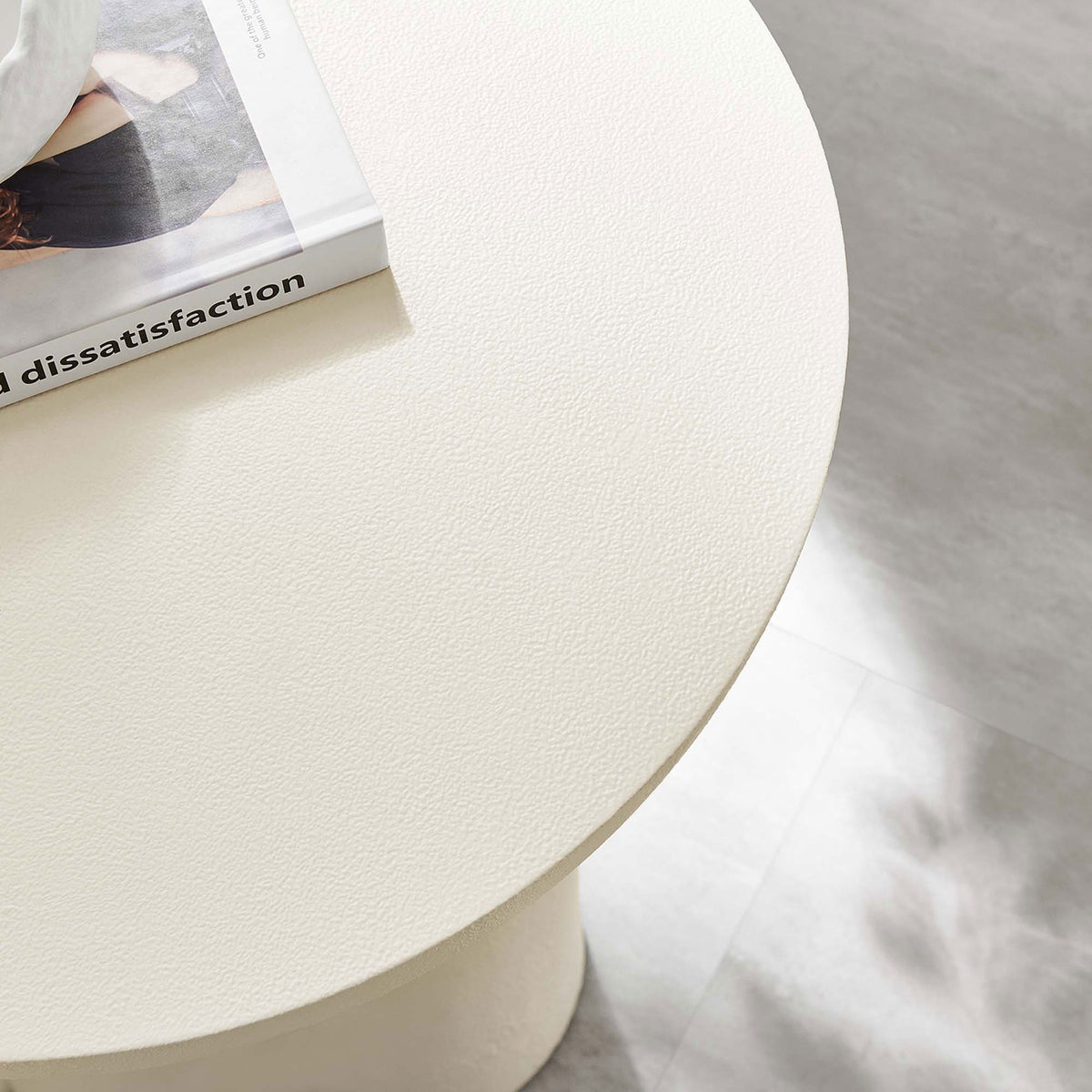 Textured white tabletop surface styled with a book adds modern character beside a sofa in a bright living room || EEI-6761-WHI || detail_room