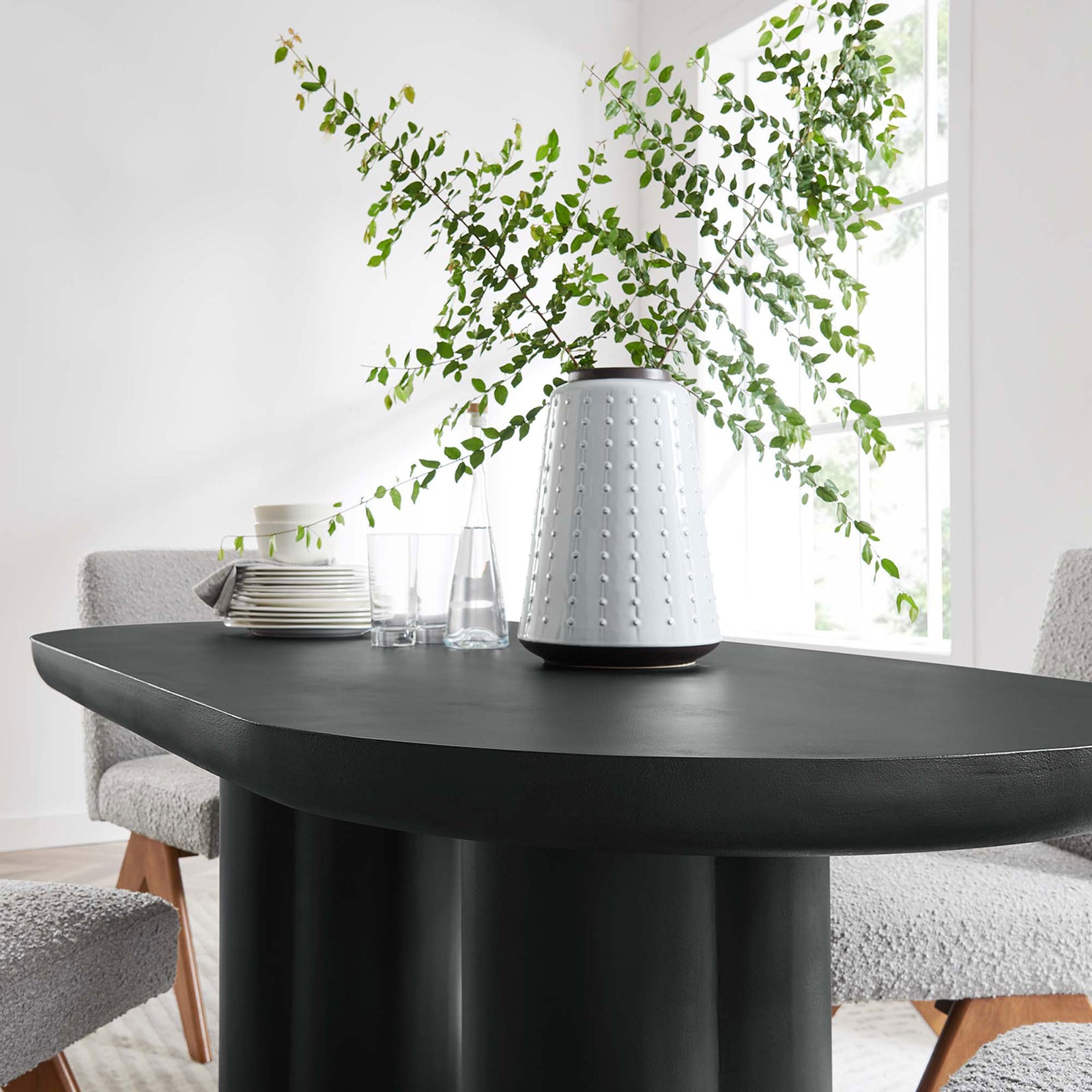 Black oval dining table styled with greenery, plates, and glassware on a sculptural base || EEI-6764-BLK || front_angle_room